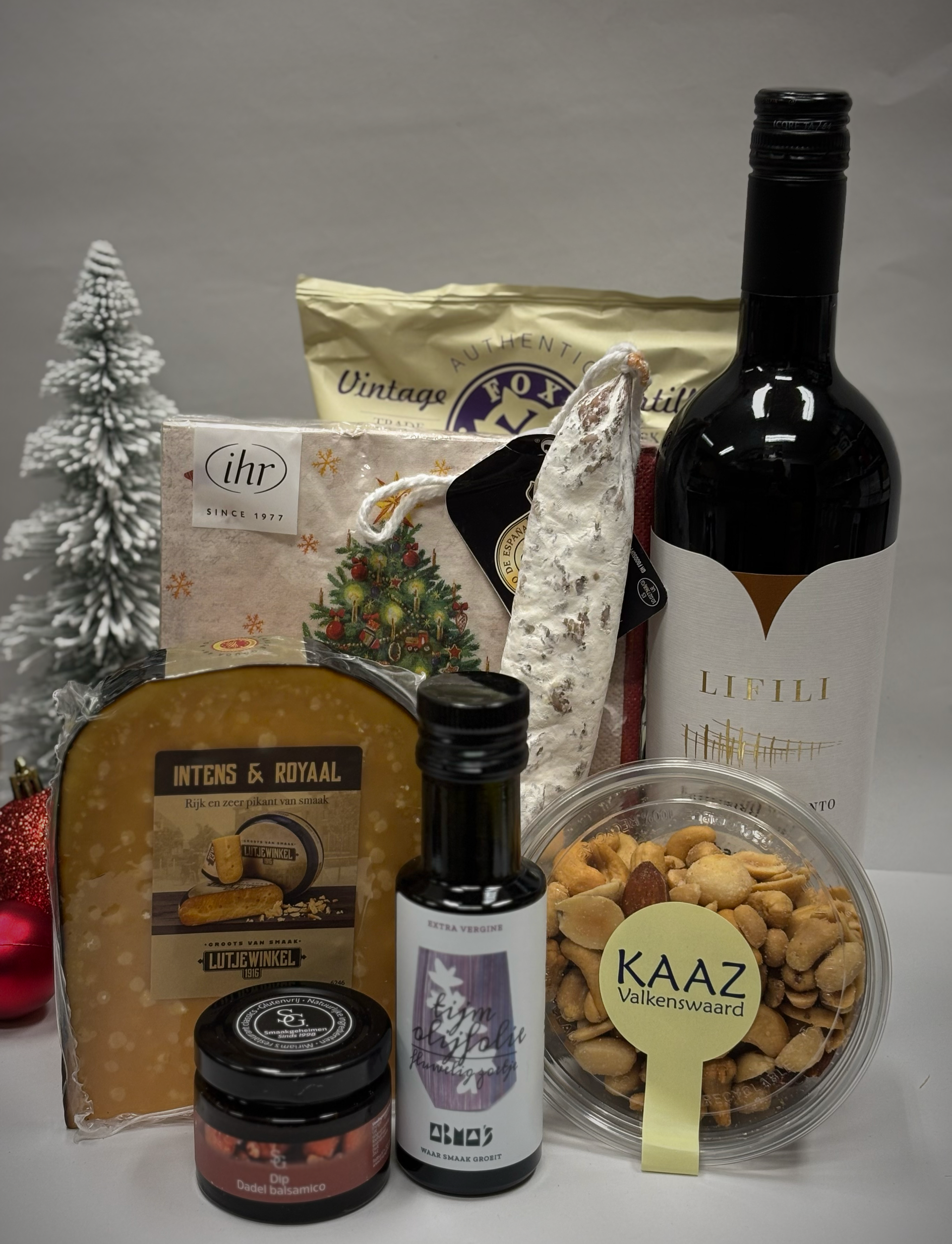 Geschenkmand met wijn, kaas, worst, crackers en snacks, met een kleine kerstboom.