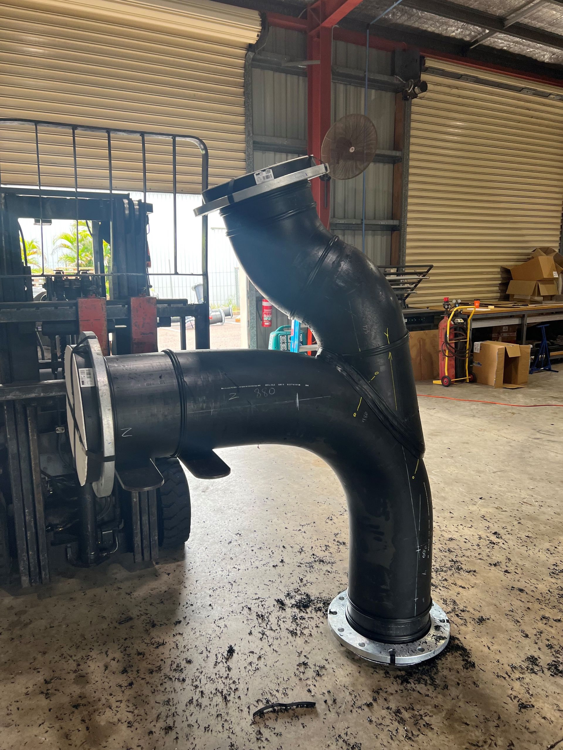 Large black industrial pipe elbow installed in a warehouse workshop, with bolts and debris on the floor. — Advanced Poly in Darwin, NT