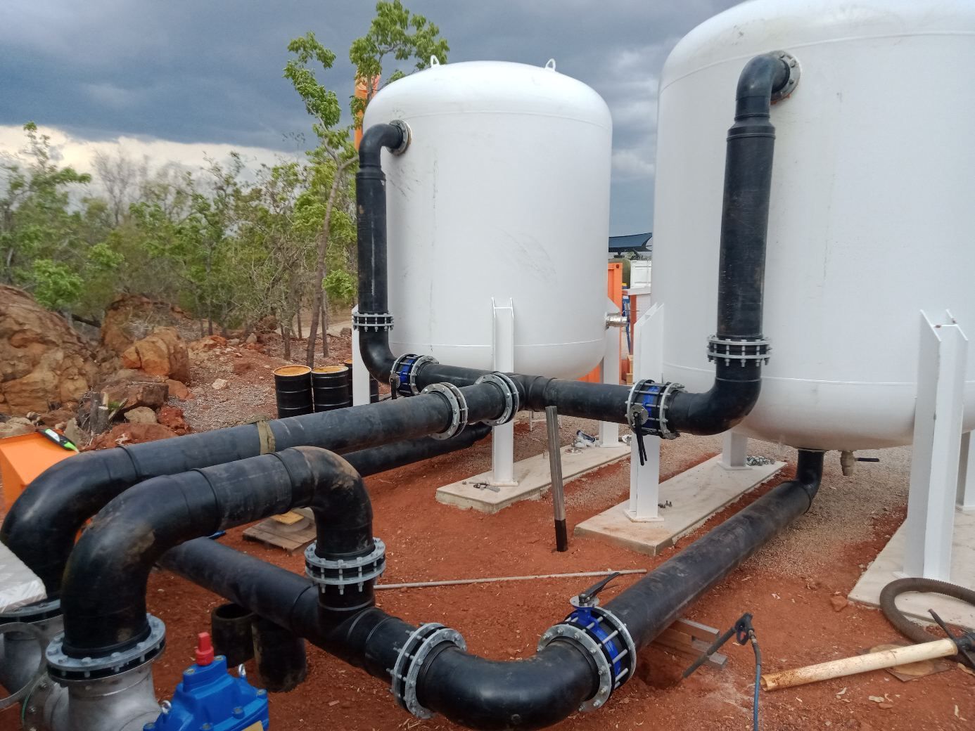 Two white industrial tanks with black pipes and valves outdoors on a rocky site — Advanced Poly in Darwin, NT