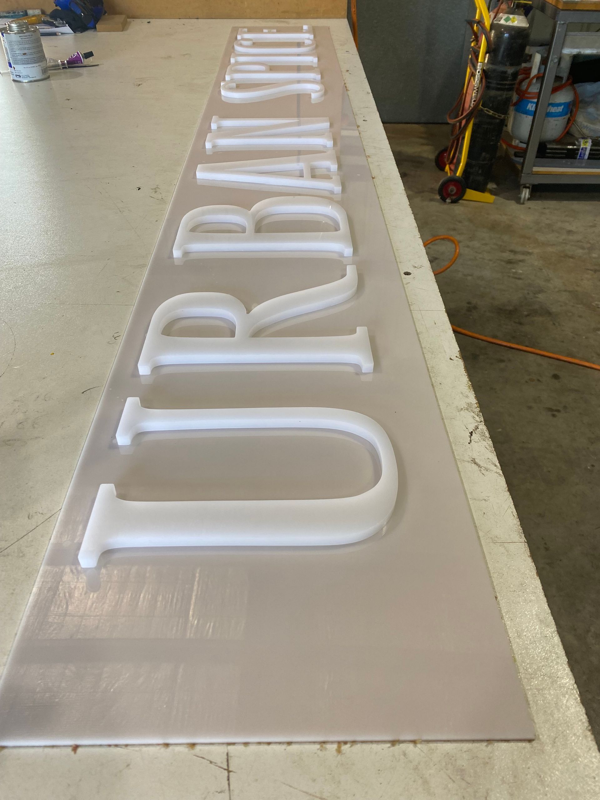 White illuminated Urodinamia letters on a long beige sign panel in a workshop. — Advanced Poly in Darwin, NT — Advanced Poly in Darwin, NT