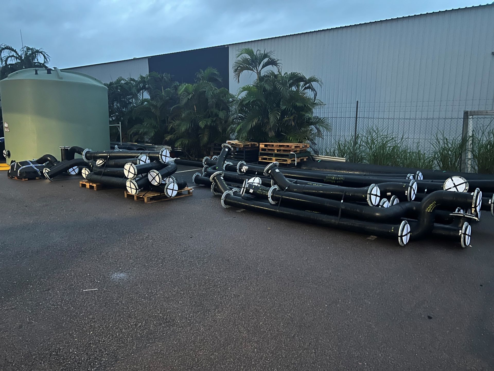 Stacks of black pipes and rolled materials stored outside an industrial building. — Advanced Poly in Darwin, NT