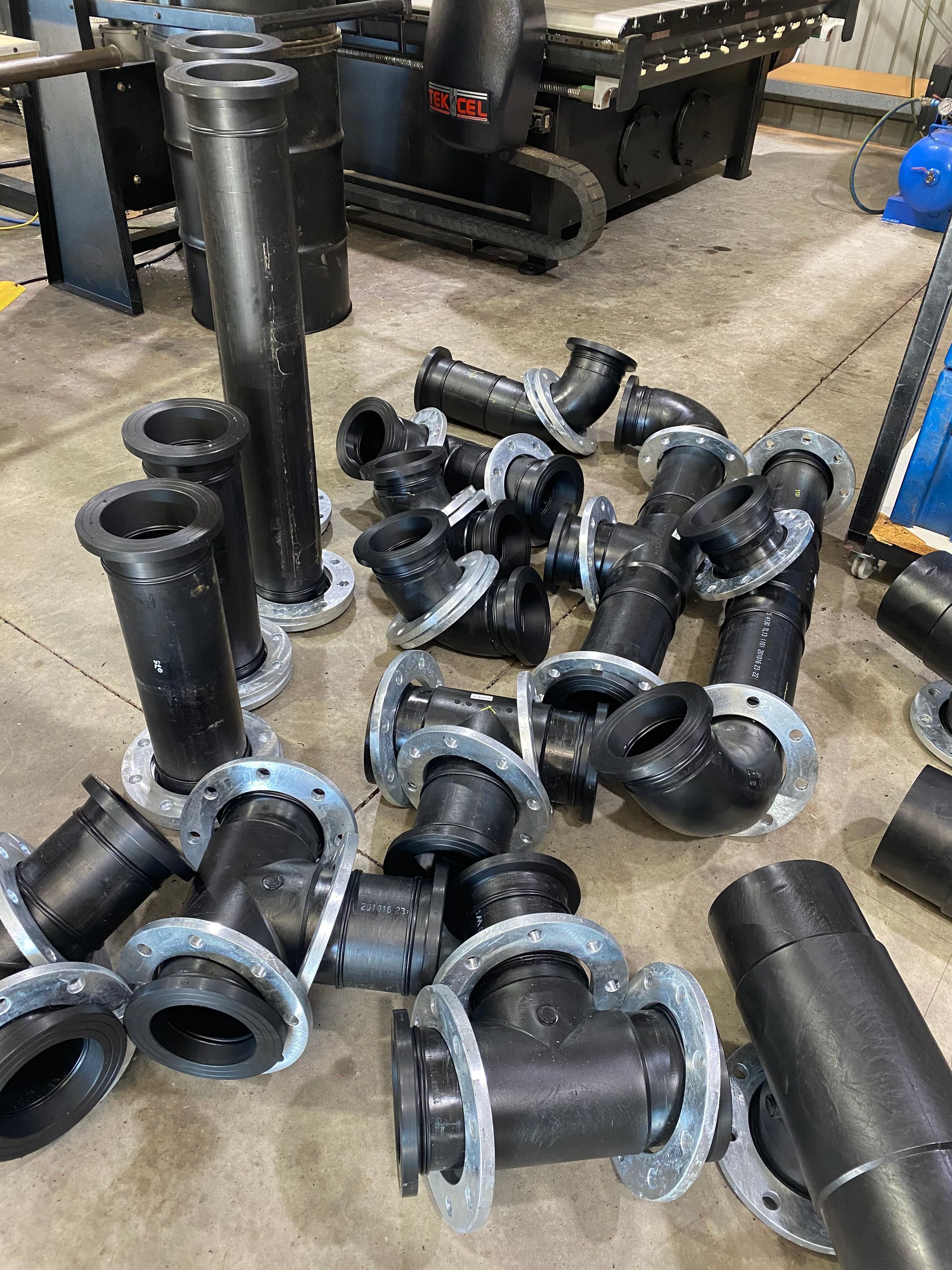 Pile of black metal pipe fittings and couplings on a workshop floor — Advanced Poly in Darwin, NT
