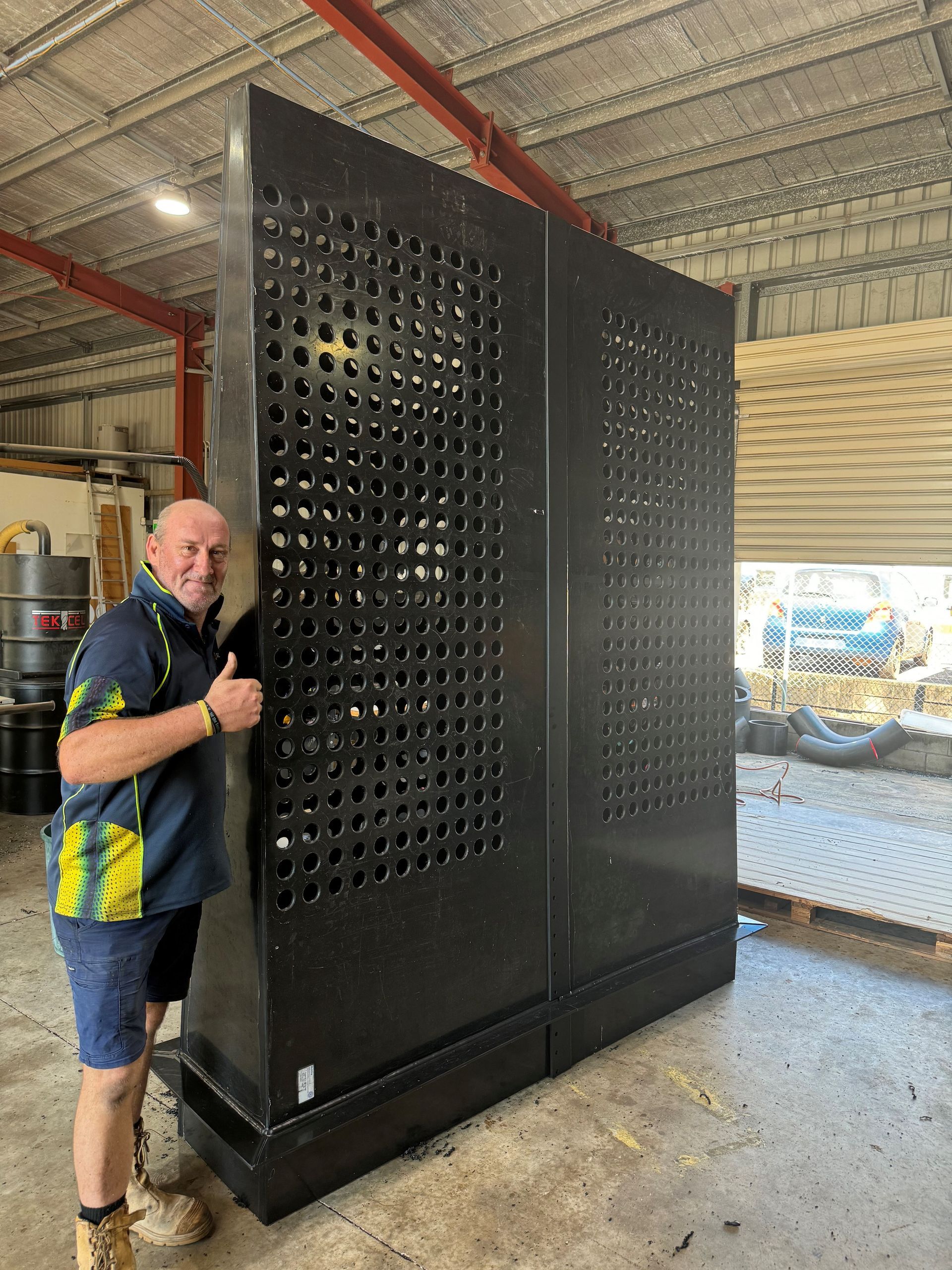 Man standing beside a large black perforated metal enclosure in a warehouse — Advanced Poly in Darwin, NT