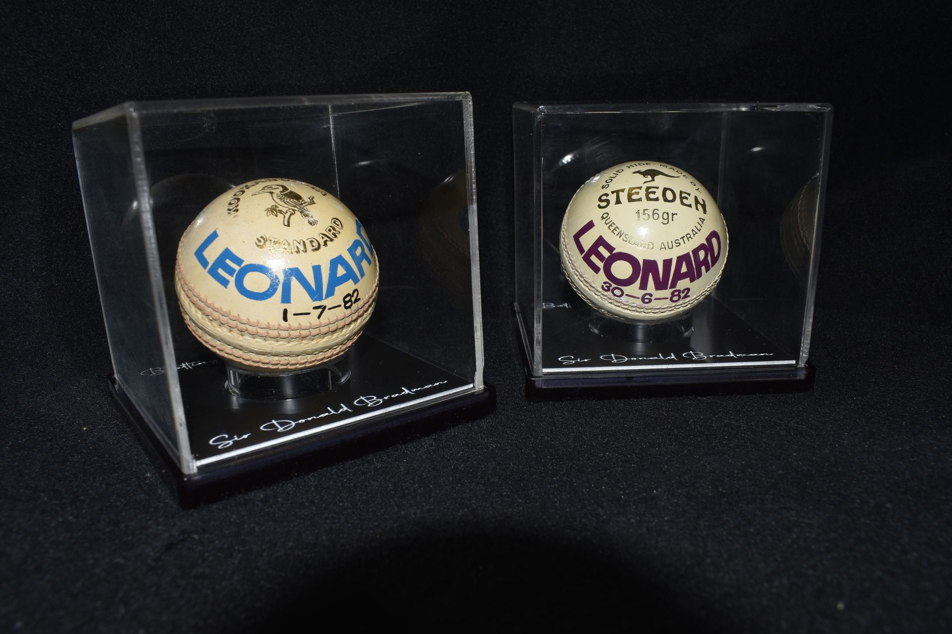 Two tennis balls displayed in clear acrylic cases on a black surface. — Advanced Poly in Darwin, NT
