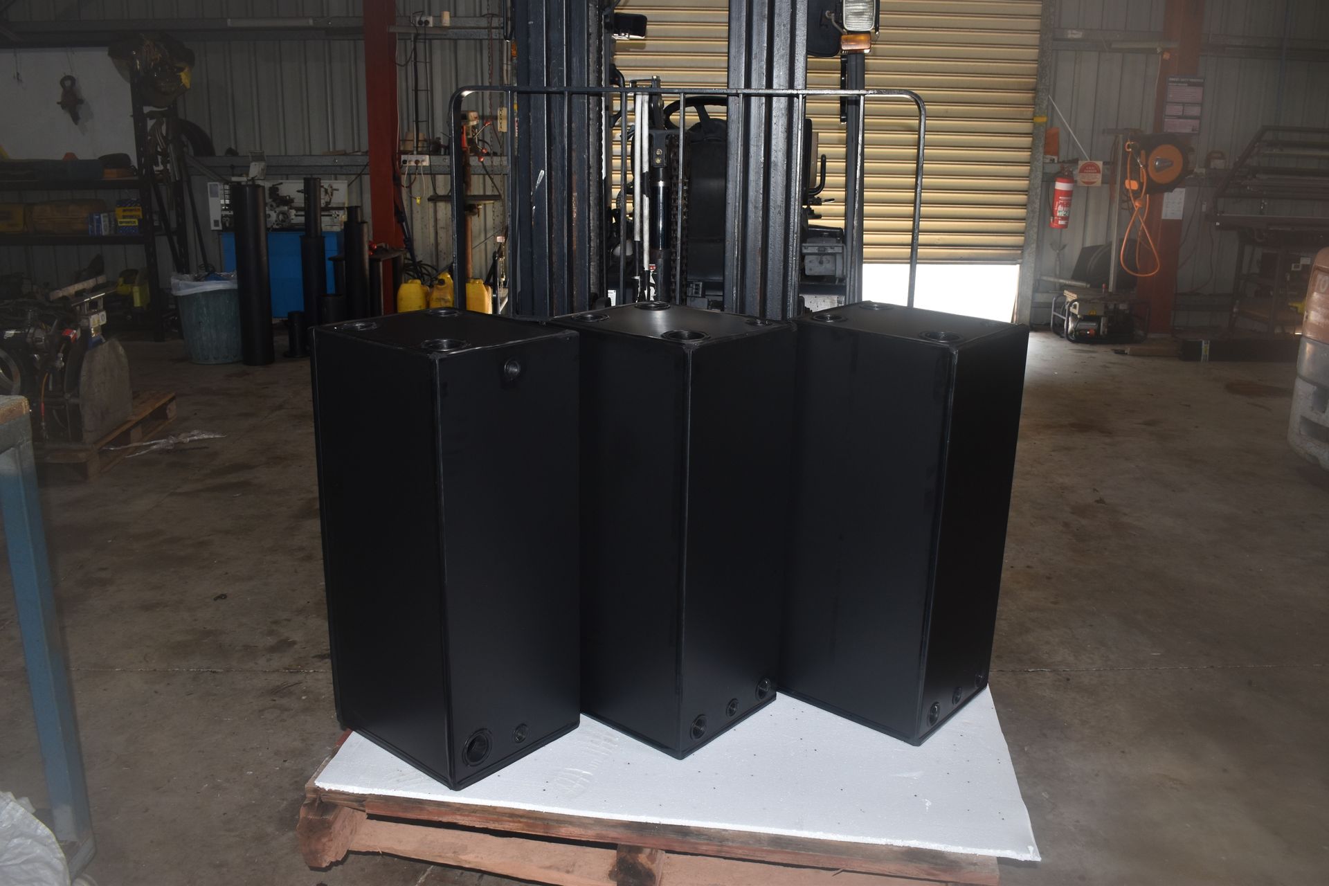 Three black cabinet speakers on a white pallet in a warehouse workshop — Advanced Poly in Darwin, NT