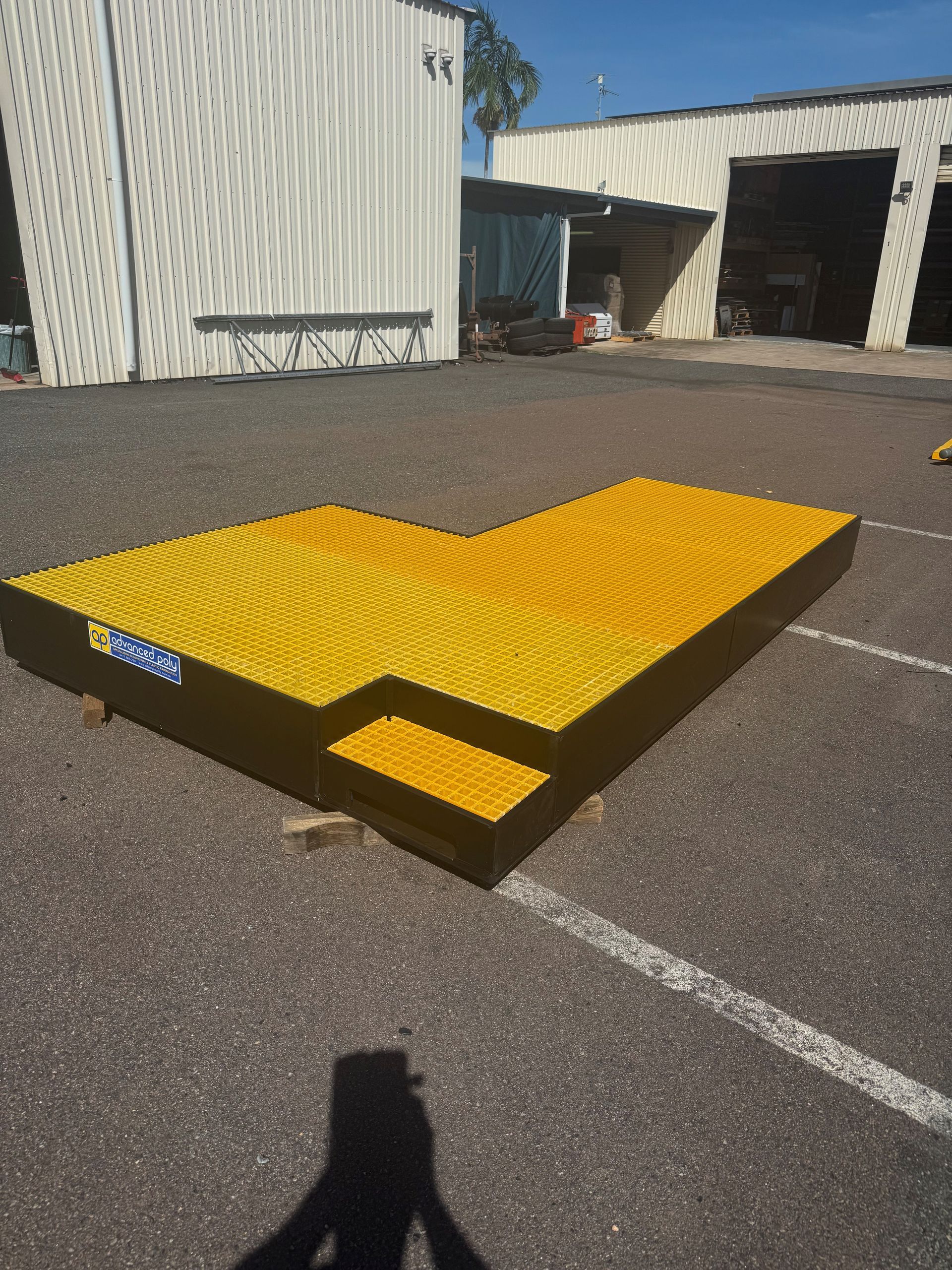 Yellow steel loading dock ramp with black frame on asphalt outside a warehouse — Advanced Poly in Darwin, NT
