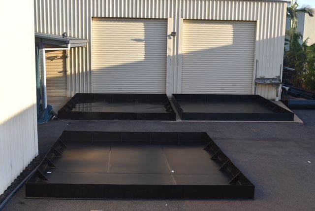 Outdoor loading area with black metal ramps and platforms in front of a corrugated building with two roll-up doors — Advanced Poly in Darwin, NT 