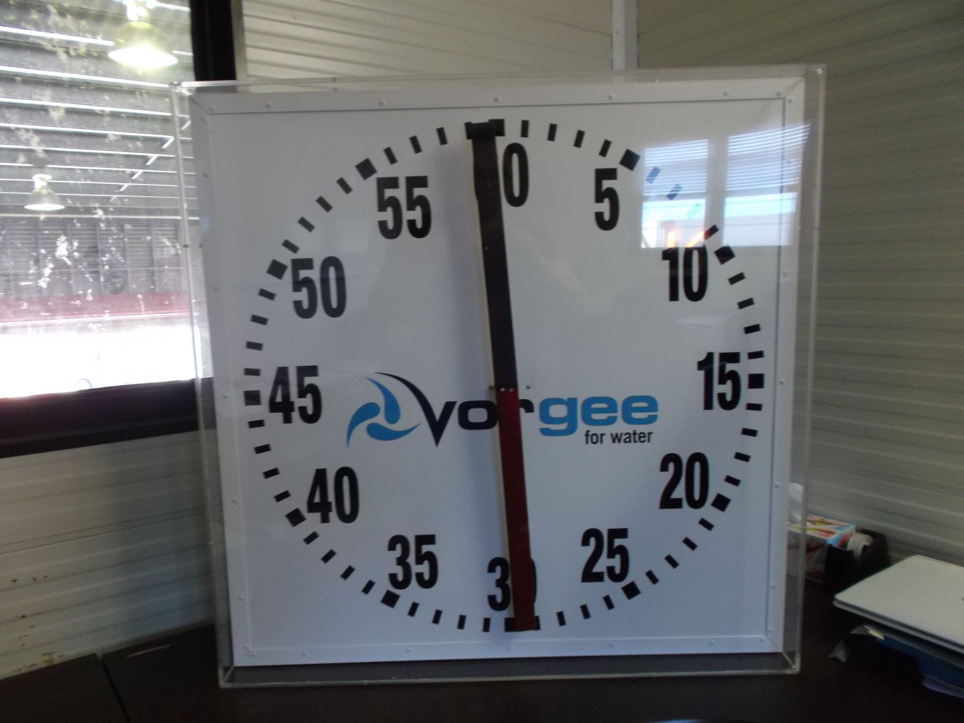 Wall clock with black numbers and hands showing about 12:30 on a white face with a blue logo — Advanced Poly in Darwin, NT