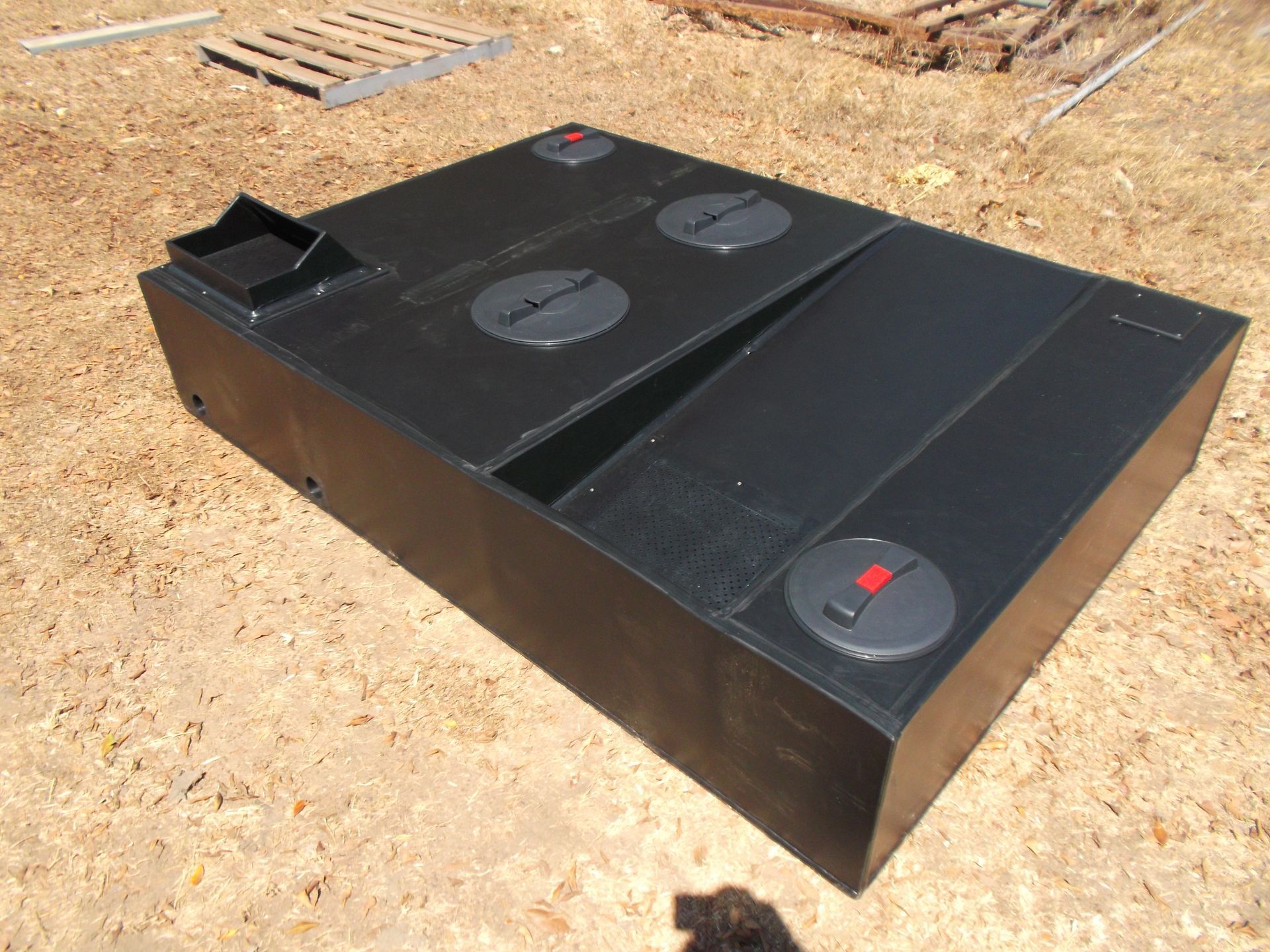 Black rectangular water tank outdoors on dirt, with a sloped top and circular access covers — Advanced Poly in Darwin, NT — Advanced Poly in Darwin, NT — Advanced Poly in Darwin, NT — Advanced Poly in Darwin, NT — Advanced Poly in Darwin, NT 