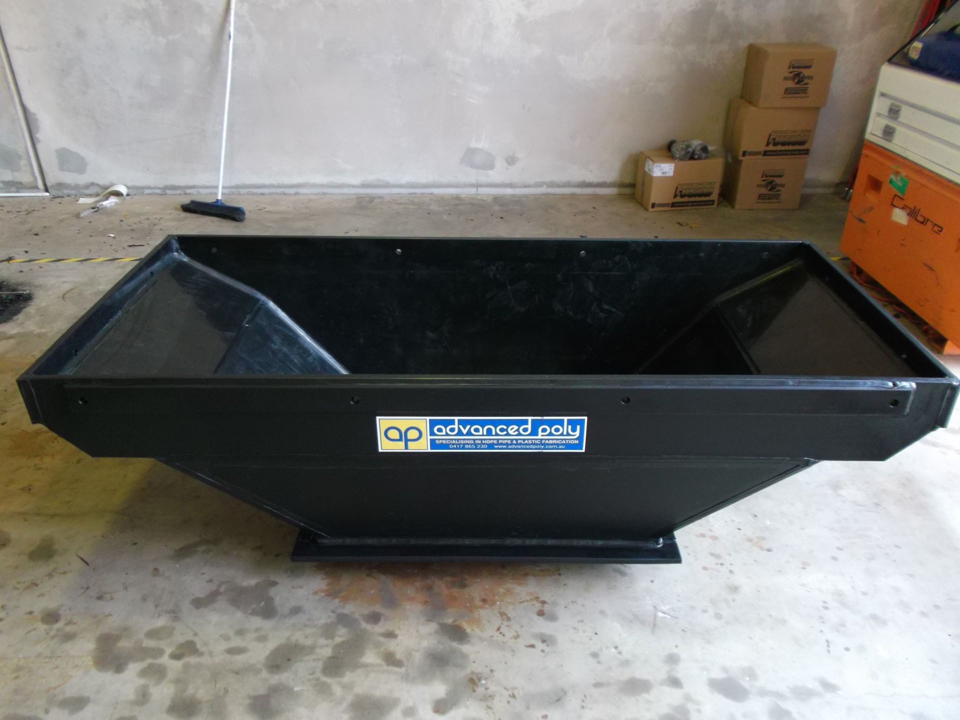 Black metal construction hopper/bin in a garage, with a white logo label on the front. — Advanced Poly in Darwin, NT