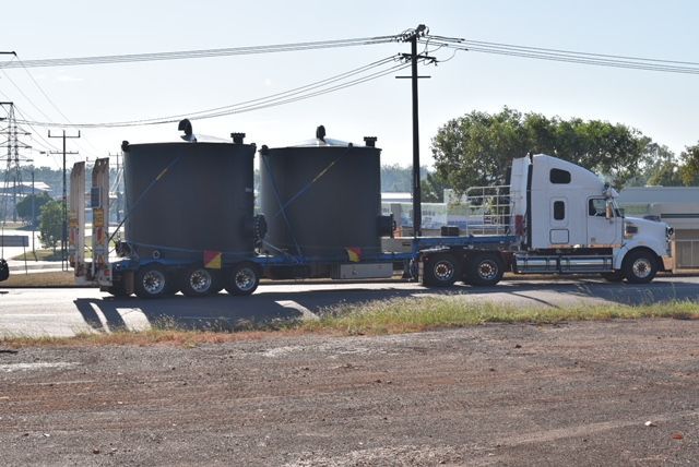White semi-truck hauling two black utility trailers on a roadside under power lines — Advanced Poly in Darwin, NT 