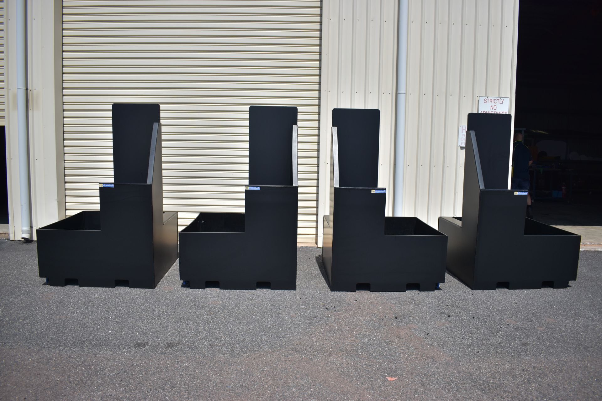 Four black chairs lined up on pavement in front of a closed metal garage door. — Advanced Poly in Darwin, NT