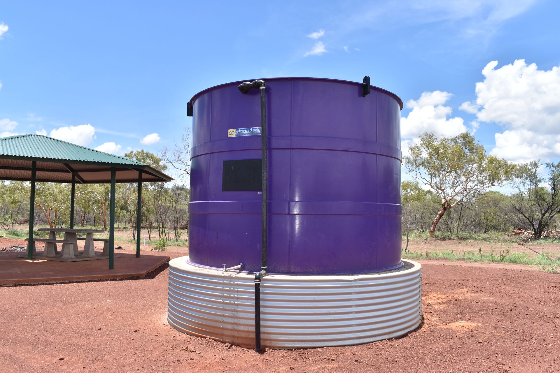 Purple water tank on corrugated metal base in a dry outdoor area with a small shelter nearby — Advanced Poly in Darwin, NT