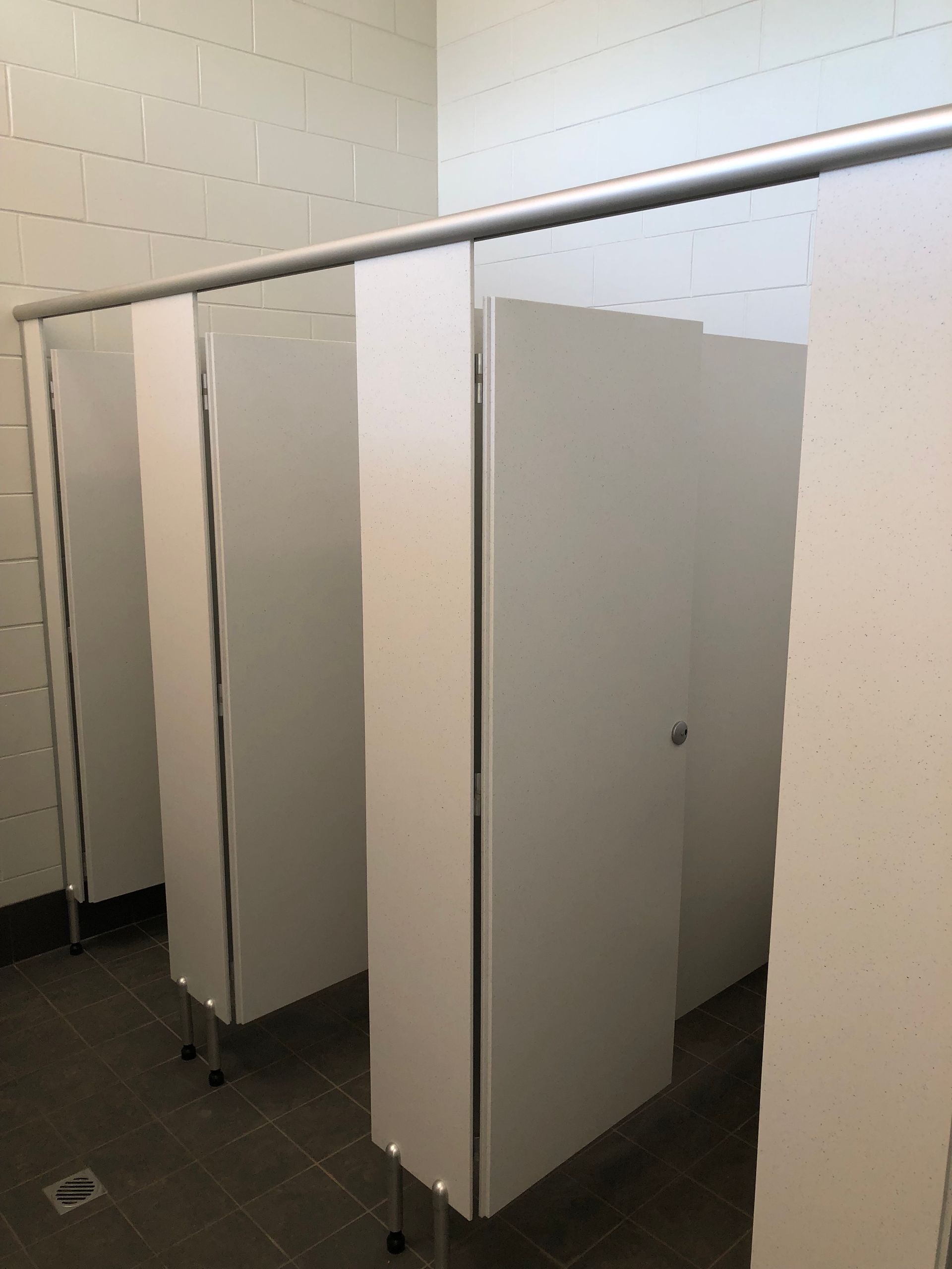 Row of empty bathroom stalls with gray partitions and white walls in a tiled restroom — Advanced Poly in Darwin, NT
