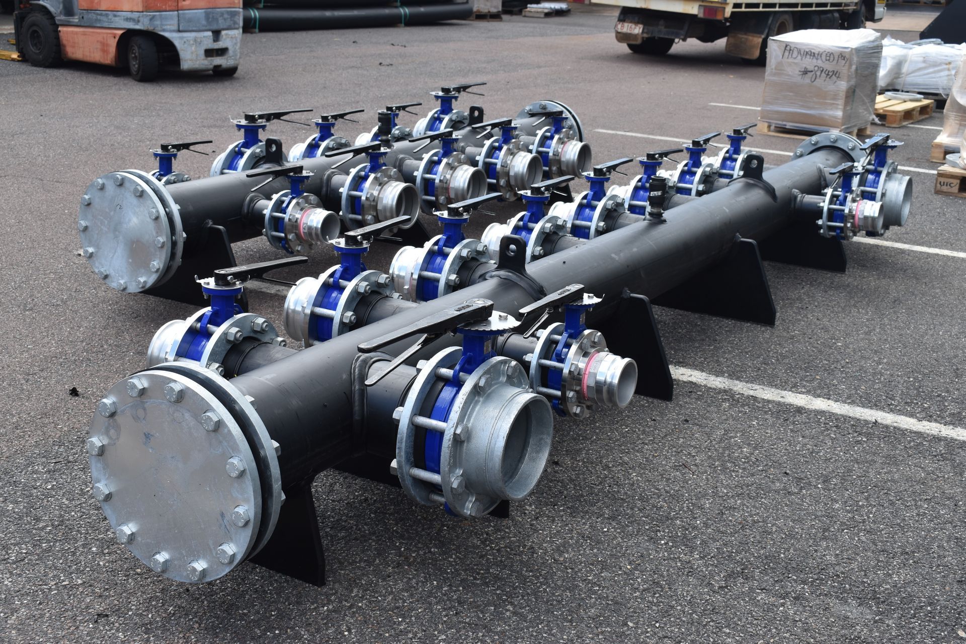 Industrial metal pipe assembly with multiple blue flanges and valves on a paved lot — Advanced Poly in Darwin, NT