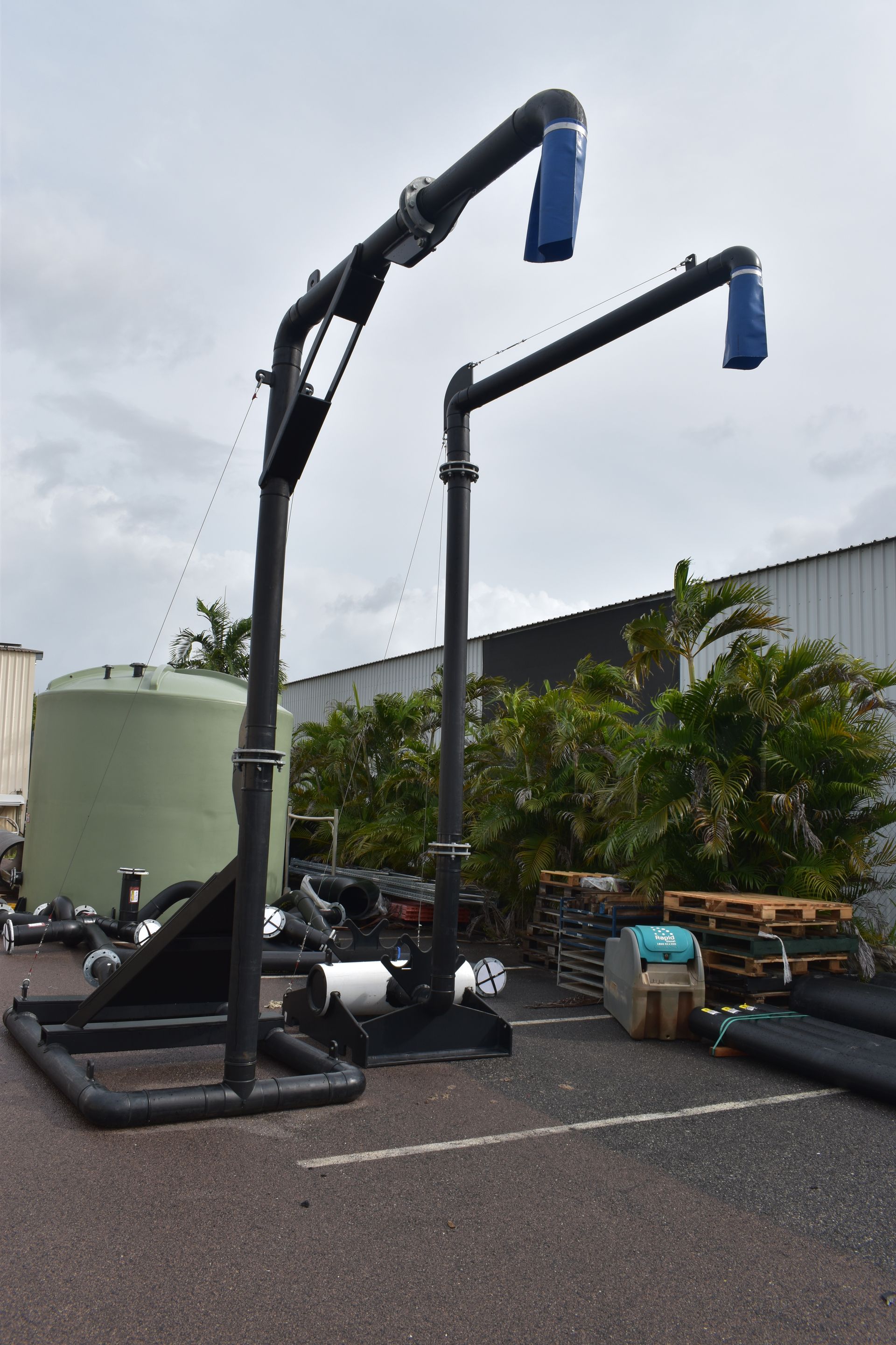 Industrial crane arms with blue covers on a rooftop or yard beside pipes and tanks under a cloudy sky — Advanced Poly in Darwin, NT