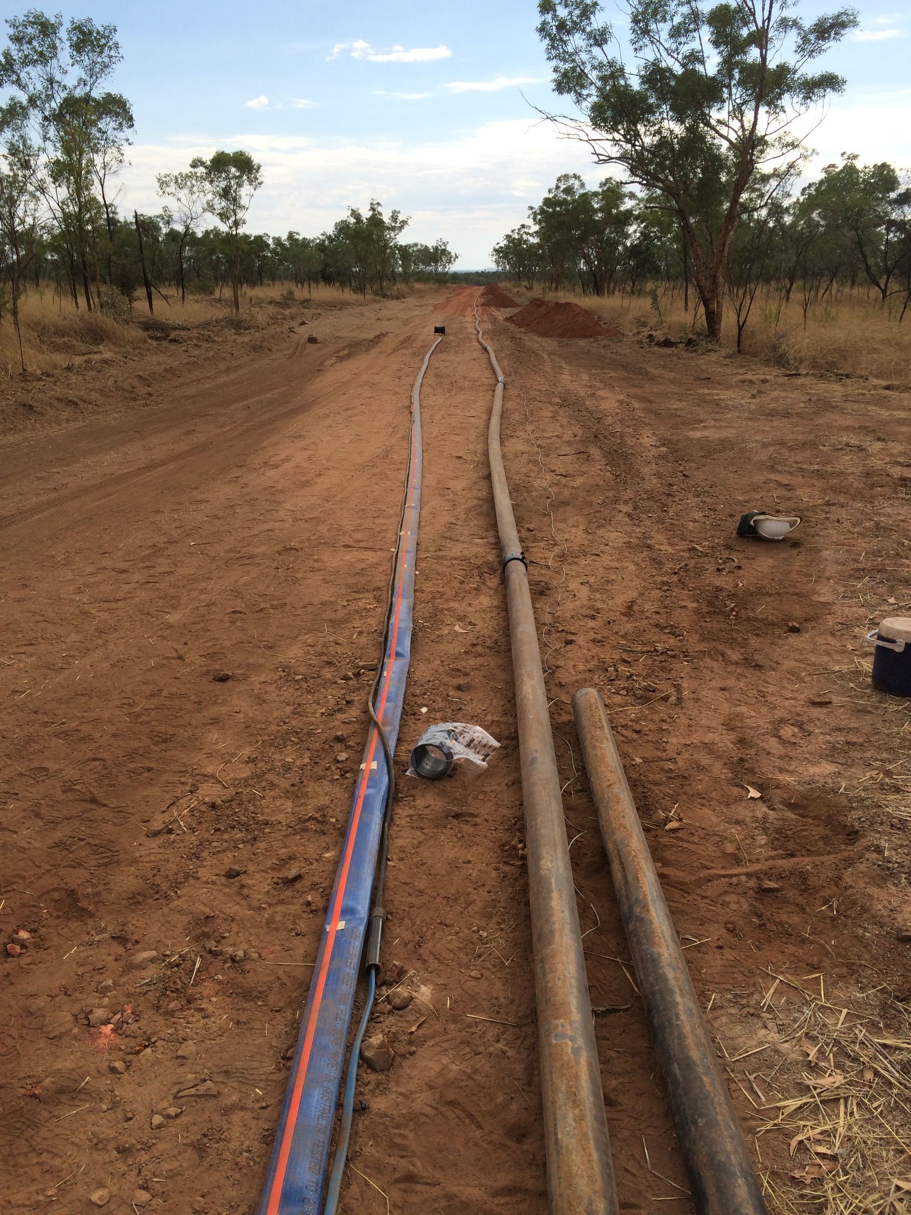 Two long pipes laid along a dirt road in a dry rural area with scattered trees. — Advanced Poly in Darwin, NT