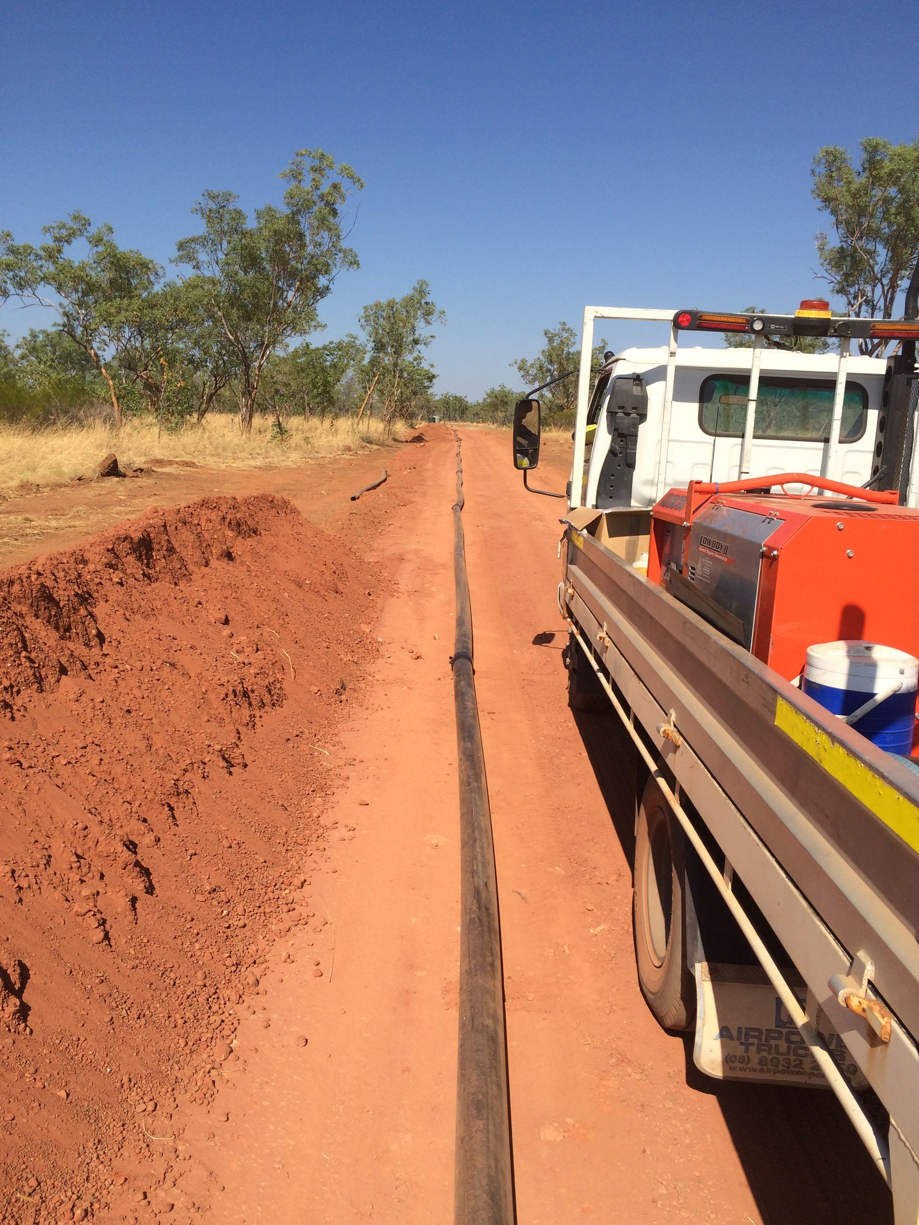 Red dirt road beside a white truck carrying an orange tank in a rural landscape. — Advanced Poly in Darwin, NT
