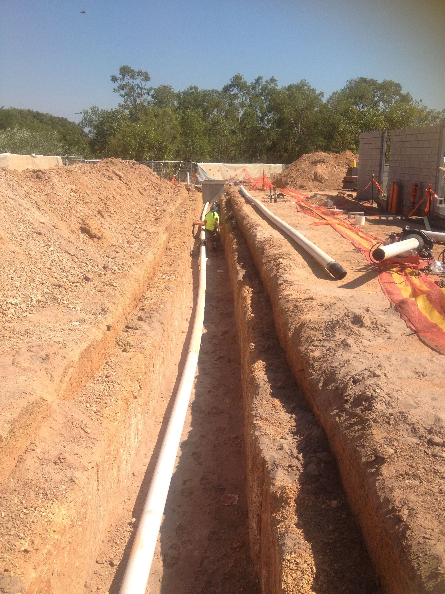 Trenched utility line installation with white pipes in a dirt excavation, workers in safety gear nearby — Advanced Poly in Darwin, NT