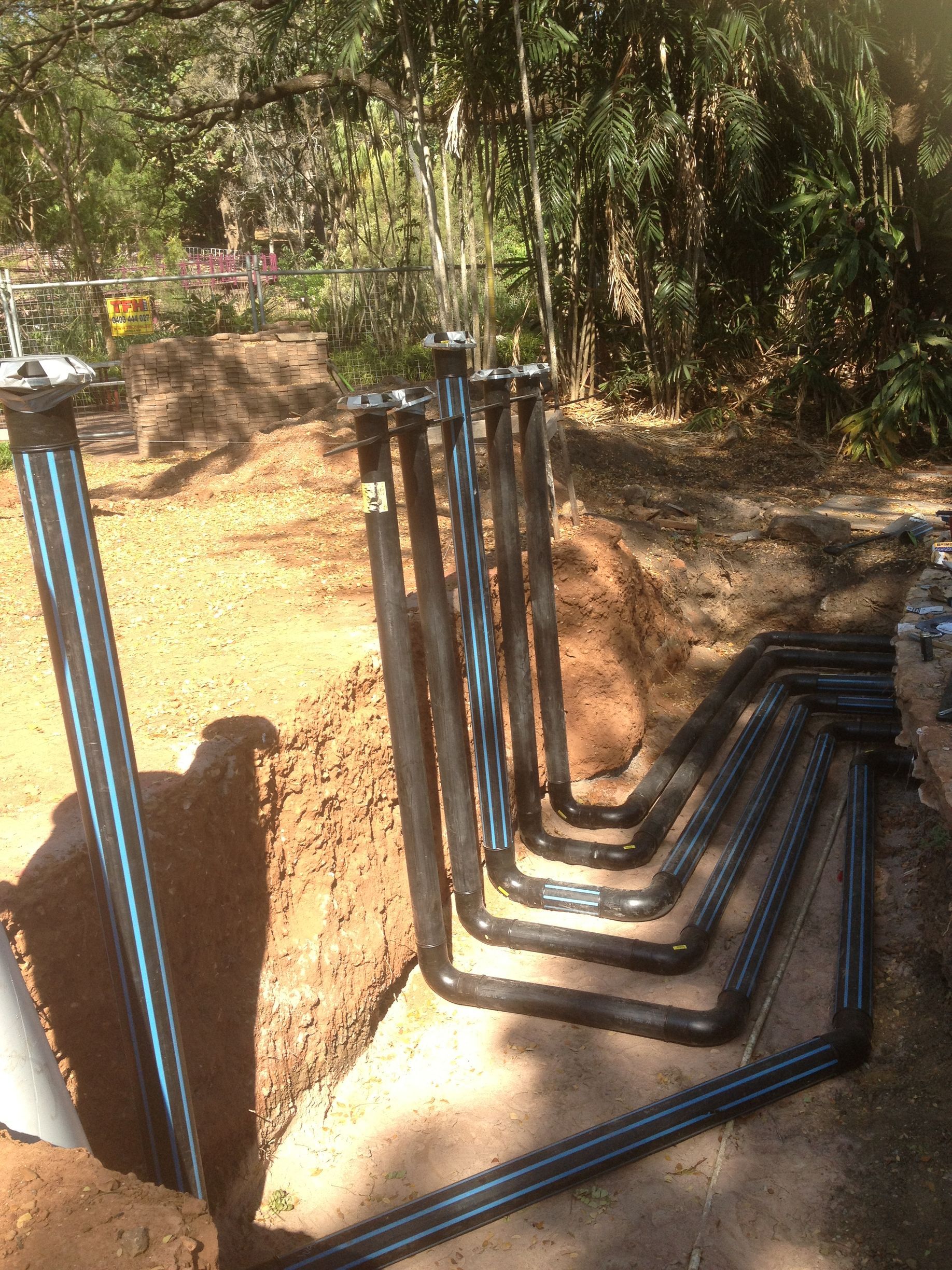 Black utility pipes laid in an L-shaped trench beside a dirt path in a wooded area — Advanced Poly in Darwin, NT