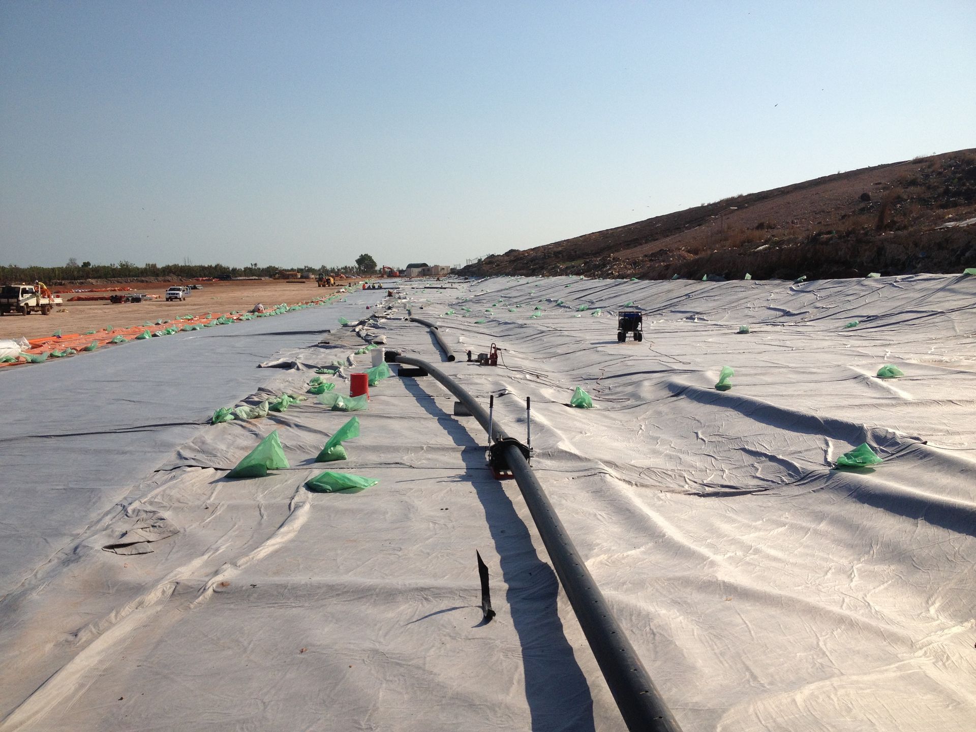 Construction site with white ground cover, hoses, and green markers stretching into the distance under a clear sky — Advanced Poly in Darwin, NT
