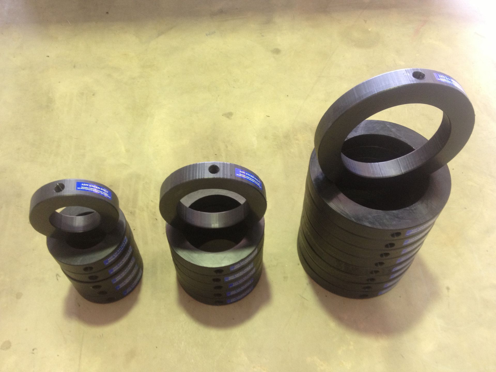 Three black metal cylindrical parts on a yellow surface, one larger ring-shaped piece standing upright. — Advanced Poly in Darwin, NT — Advanced Poly in Darwin, NT 