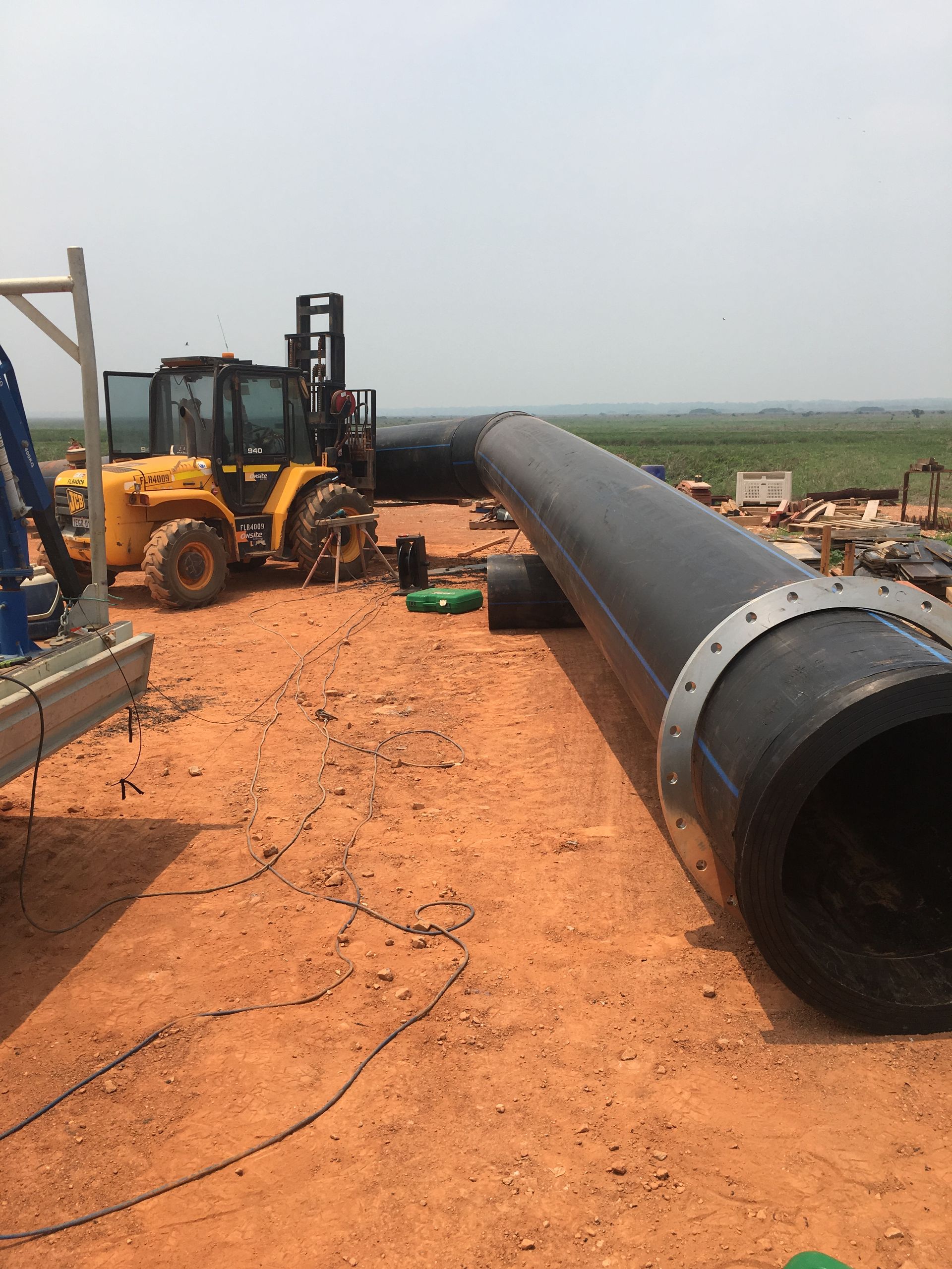 Forklift beside a large black pipeline on a red dirt construction site under a hazy sky — Advanced Poly in Darwin, NT