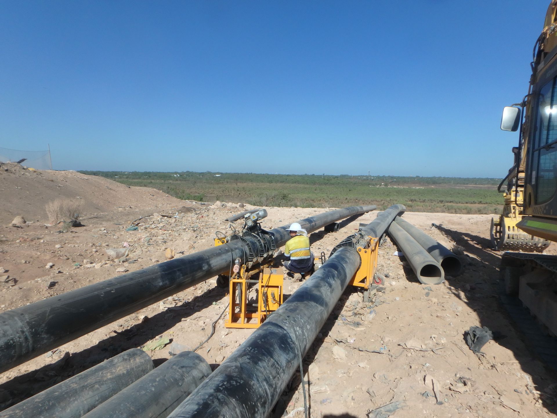 Workers handling large black pipes at a construction site under a clear blue sky — Advanced Poly in Darwin, NT