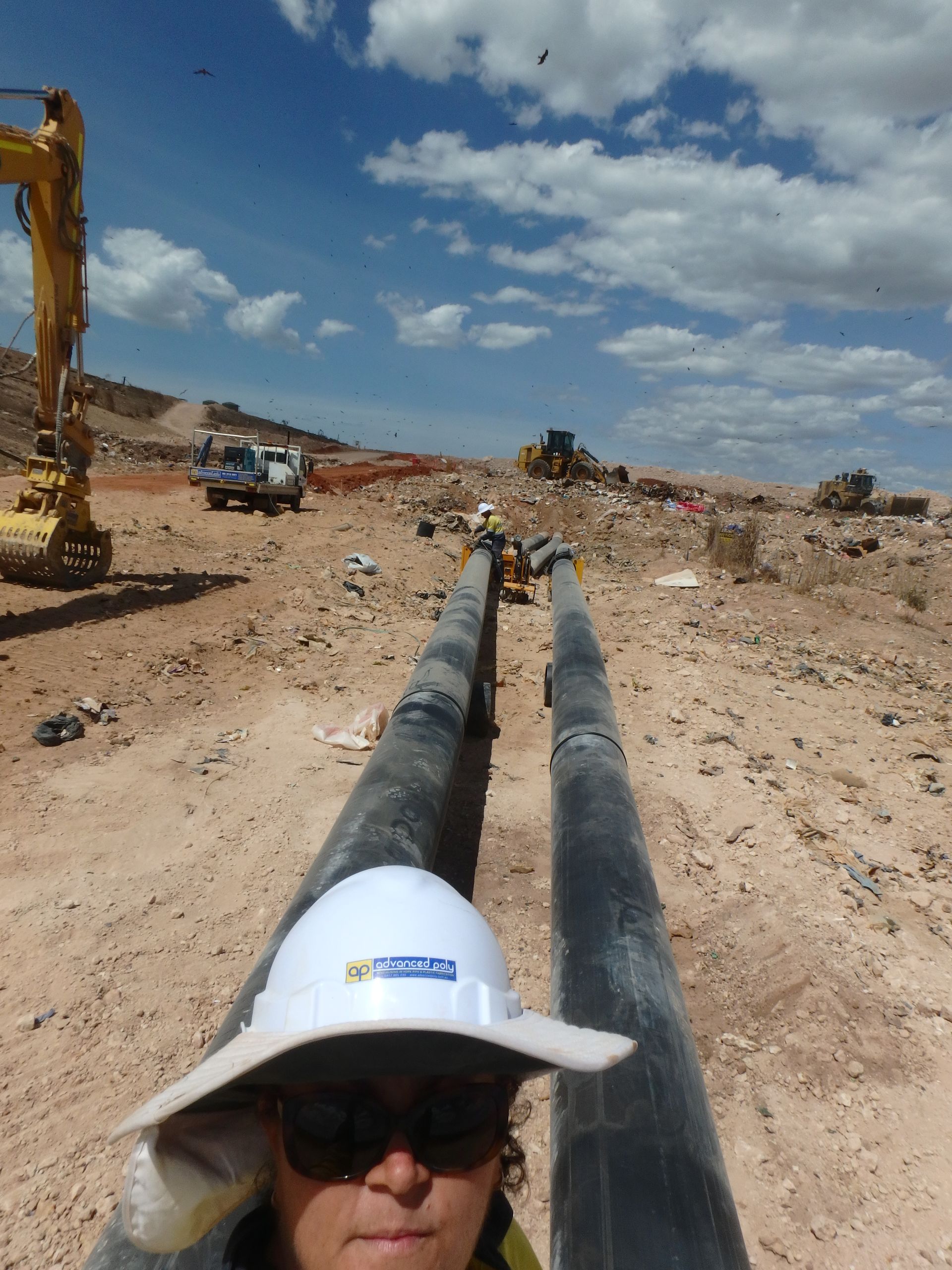 Worker in hard hat beside large black pipeline at a dusty construction site under a cloudy sky — Advanced Poly in Darwin, NT