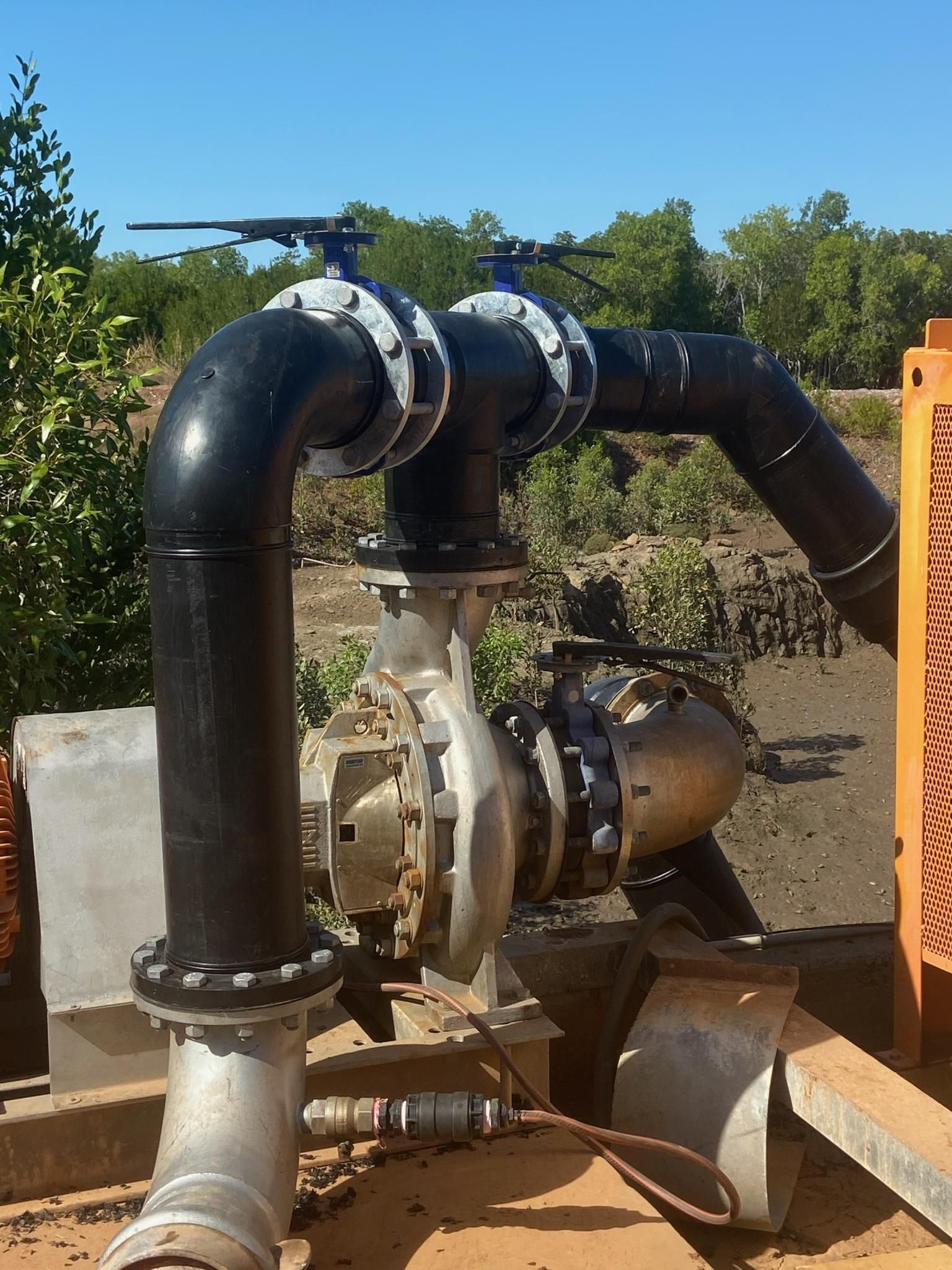 Industrial pump with black pipes and a silver motor outdoors against dirt and trees — Advanced Poly in Darwin, NT