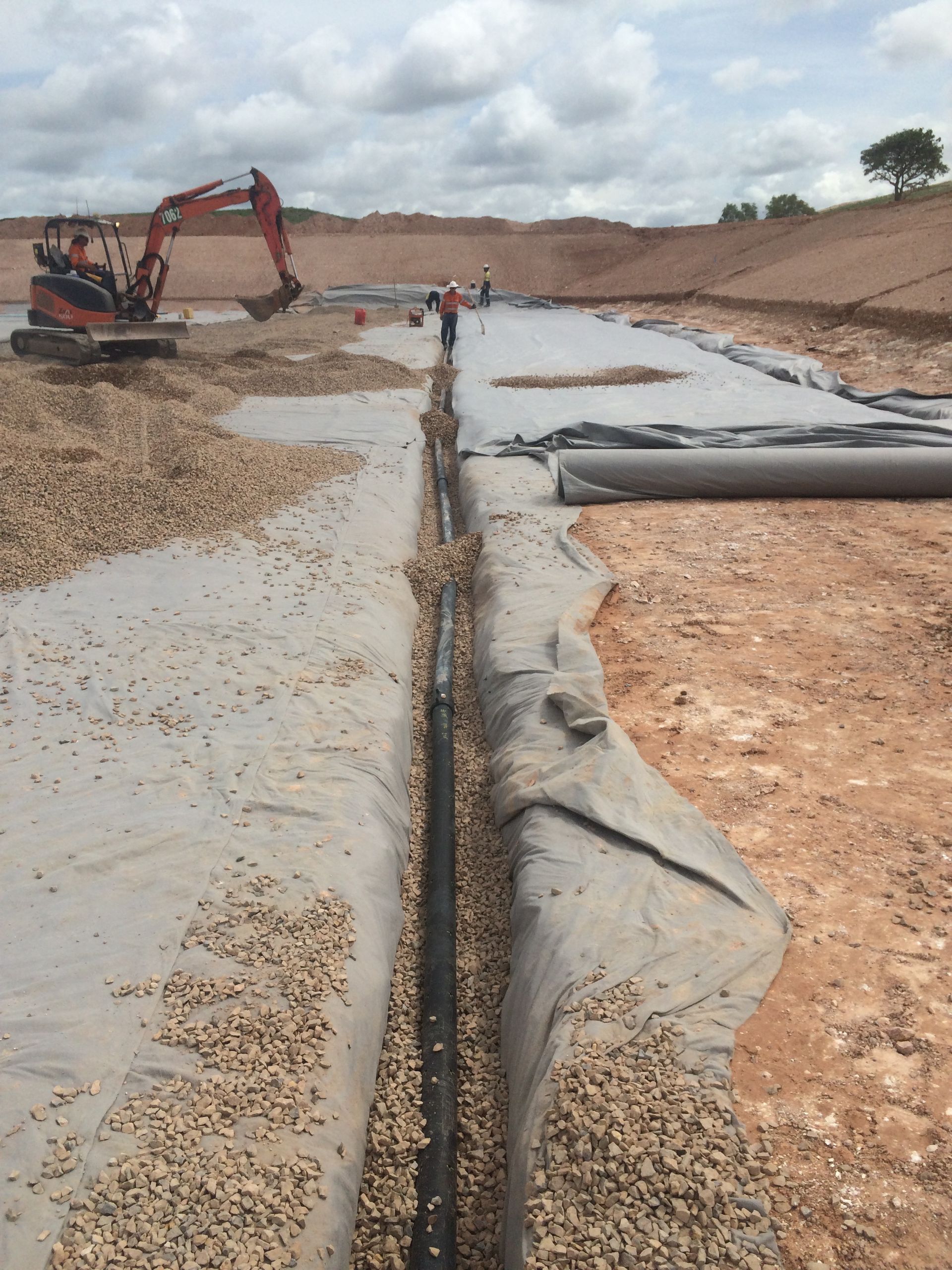 Excavator working beside a concrete-lined trench on a construction site with gravel and exposed earth — Advanced Poly in Darwin, NT