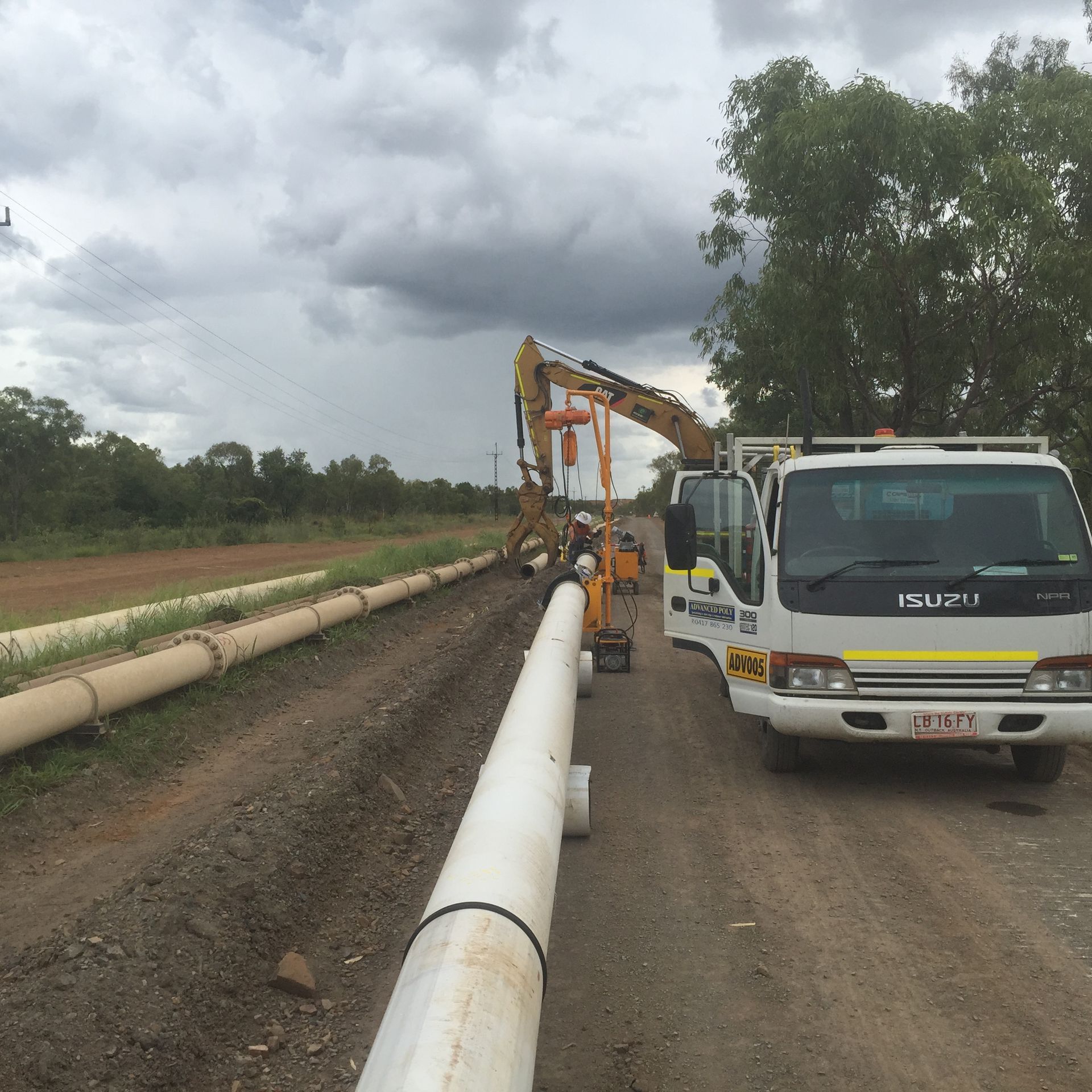 Pipeline installation beside a dirt road with a white utility truck and excavator under cloudy skies — Advanced Poly in Darwin, NT