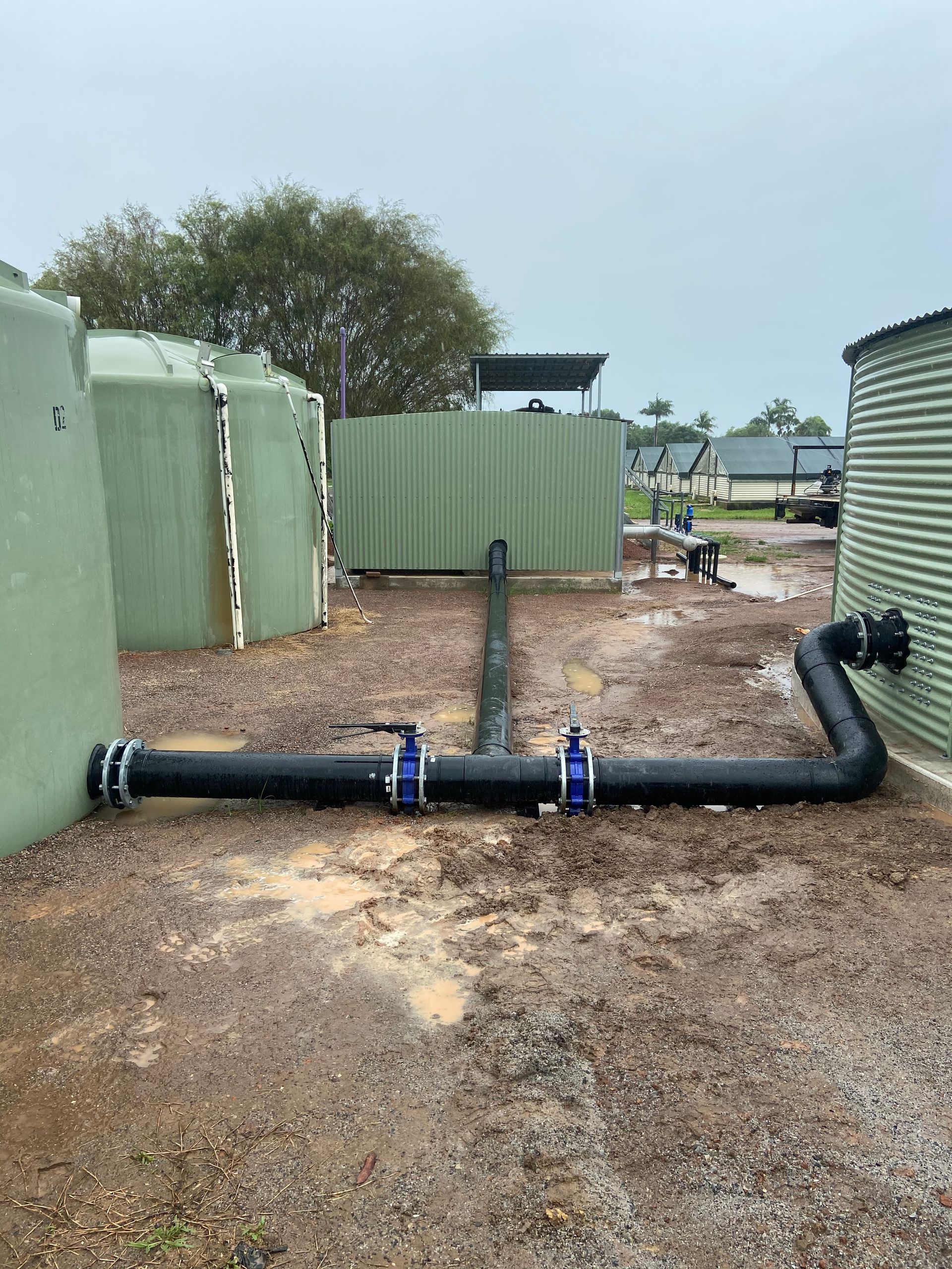 Black pipe laid across gravel between green tanks at a utility site — Advanced Poly in Darwin, NT