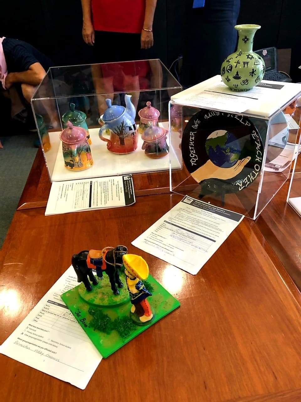 Assorted small sculptures and art pieces displayed on a wooden table with printed descriptions — Advanced Poly in Darwin, NT