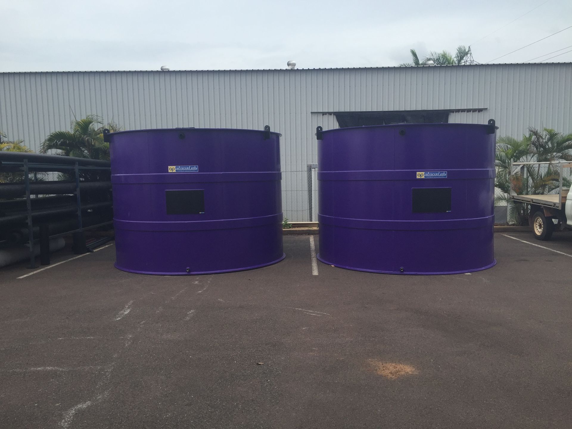 Two large purple industrial tanks on a paved lot in front of a white building. — Advanced Poly in Darwin, NT