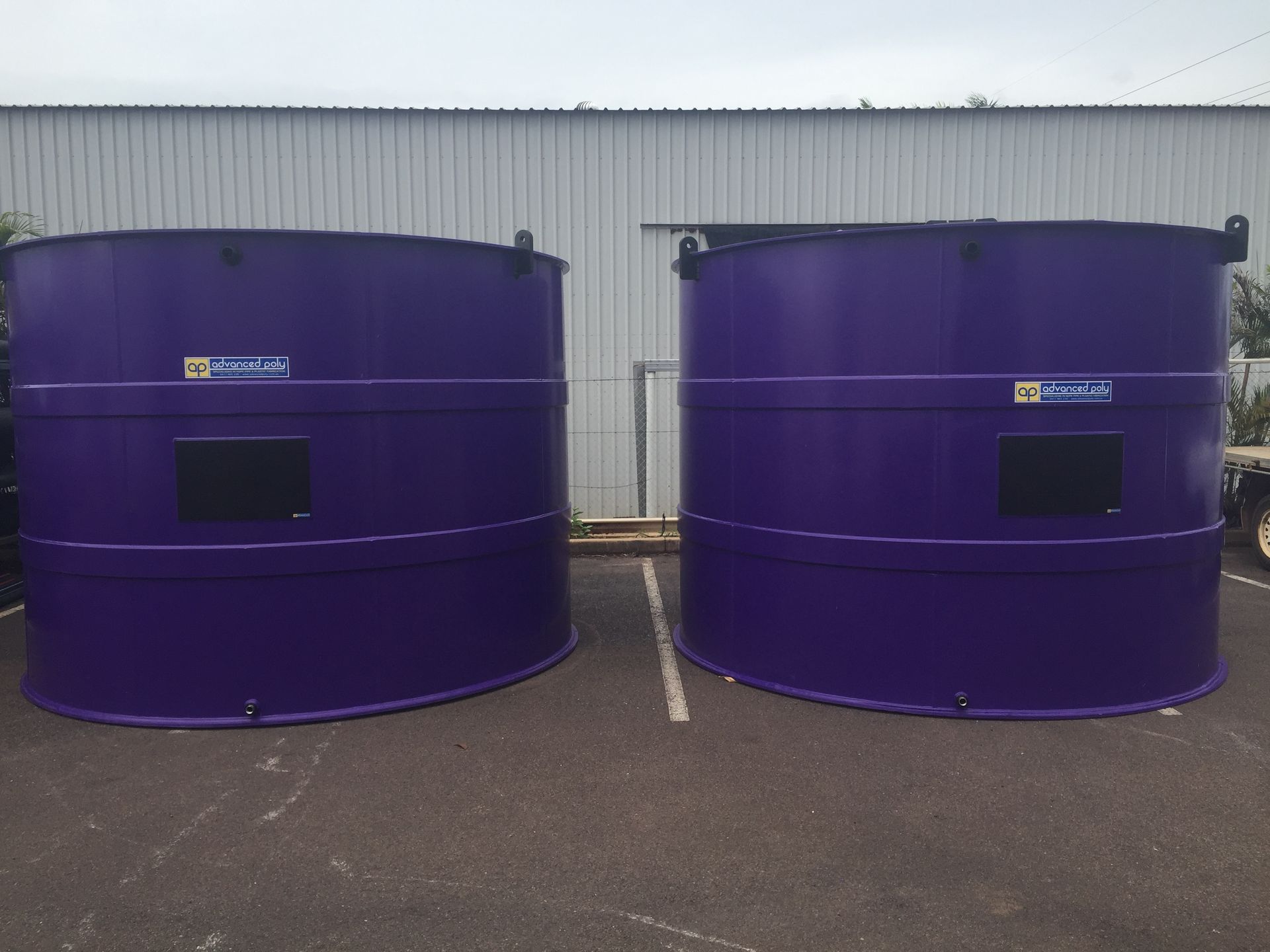 Two large purple cylindrical tanks on asphalt in front of a white metal building. — Advanced Poly in Darwin, NT