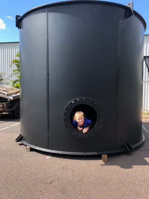 Person peering from a round opening in a large black industrial tank outdoors — Advanced Poly in Darwin, NT