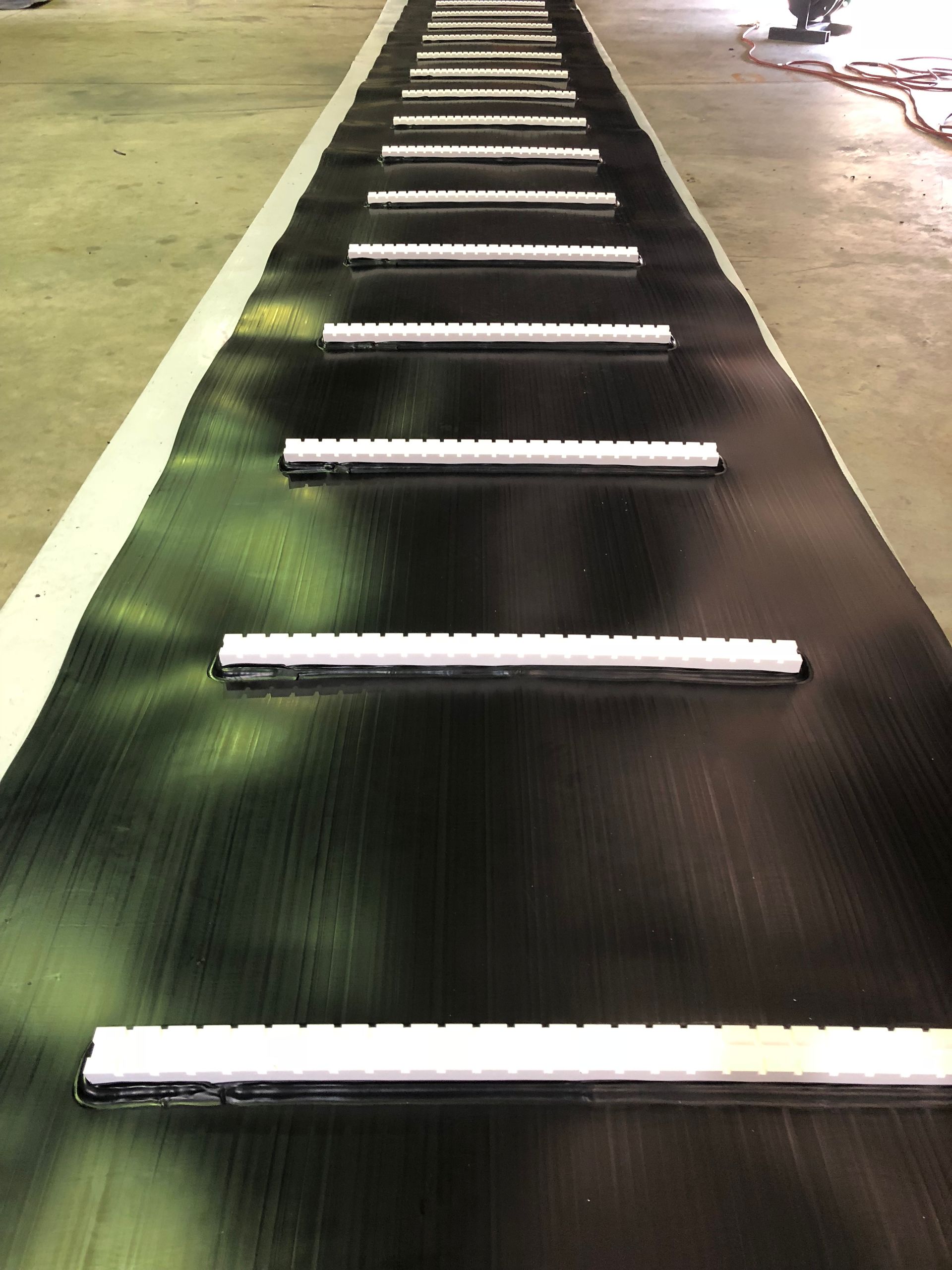 Black conveyor belt with evenly spaced white bars in an industrial setting — Advanced Poly in Darwin, NT