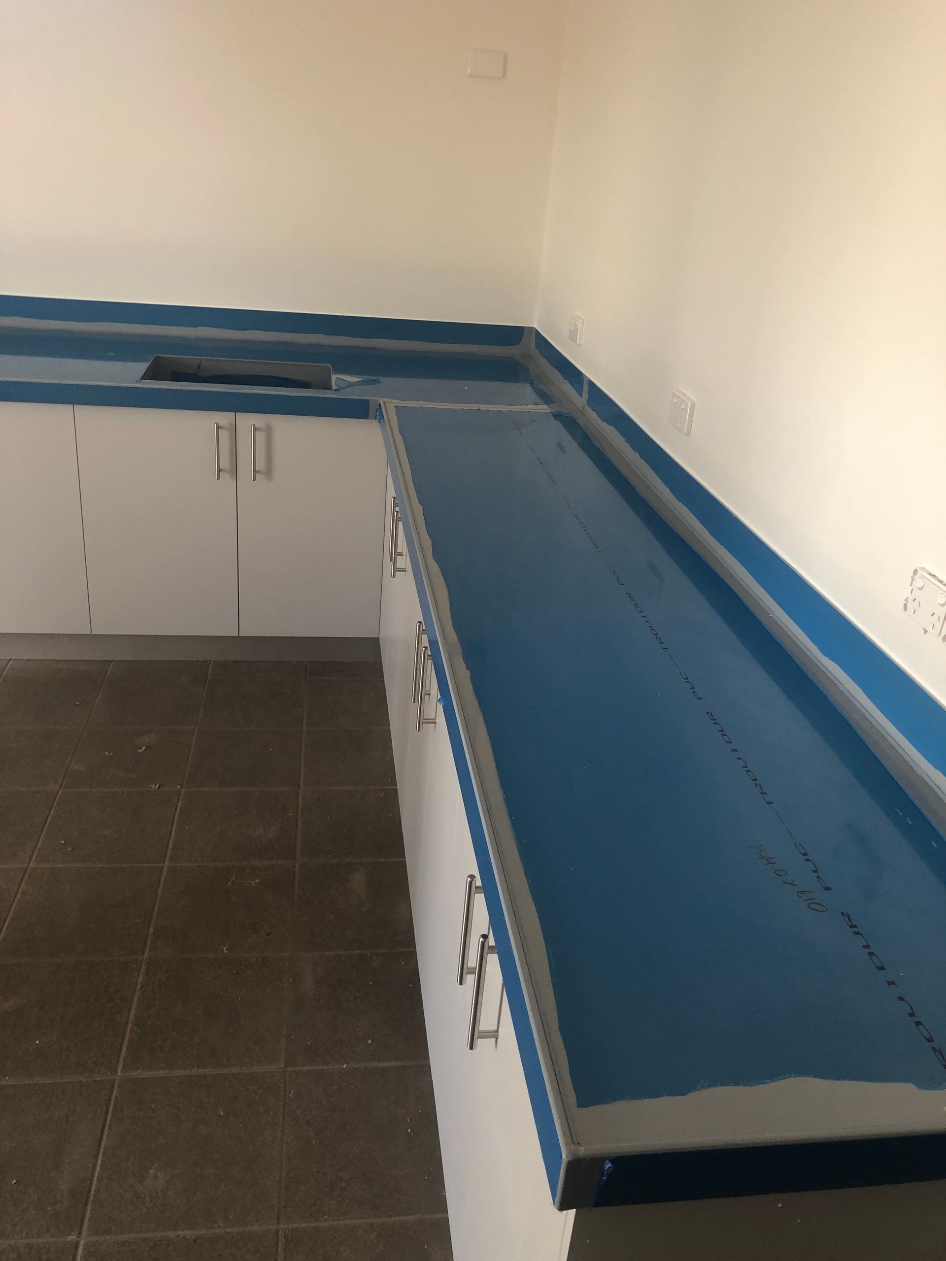 Empty kitchen with blue countertops and white cabinets, viewed from the corner. — Advanced Poly in Darwin, NT 
