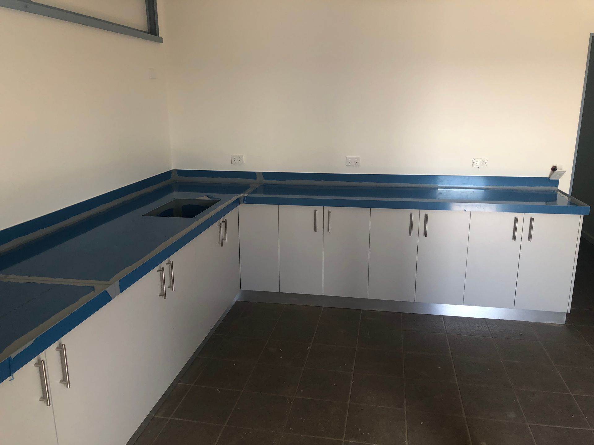 Empty kitchen corner with white cabinets, blue countertops, and dark tile floor — Advanced Poly in Darwin, NT 