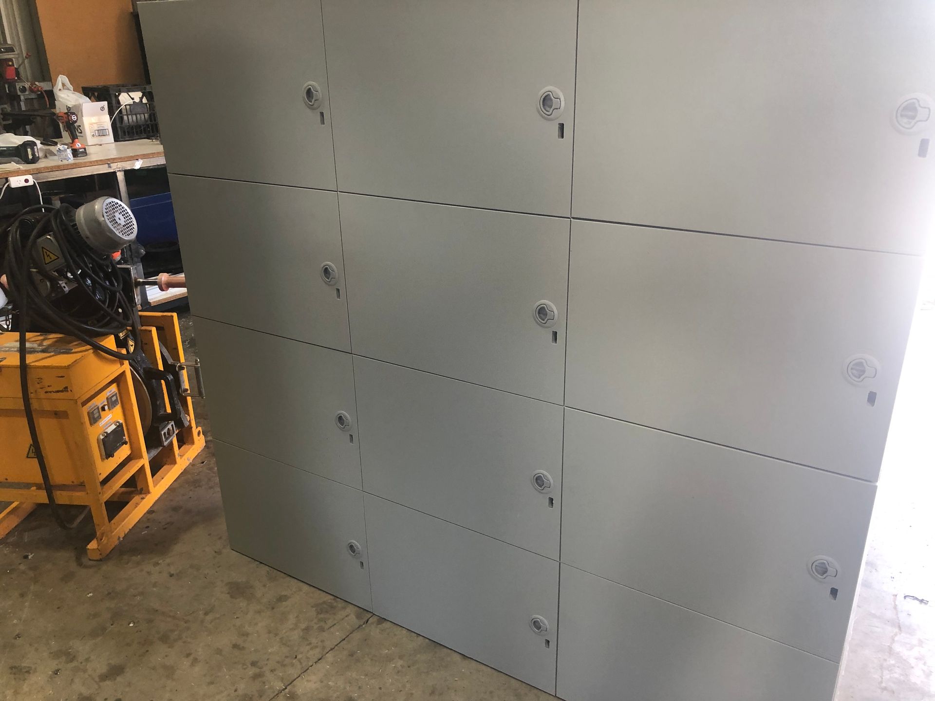 Gray metal wall panels in a workshop, with a yellow machine and shelves partially visible on the left. — Advanced Poly in Darwin, NT