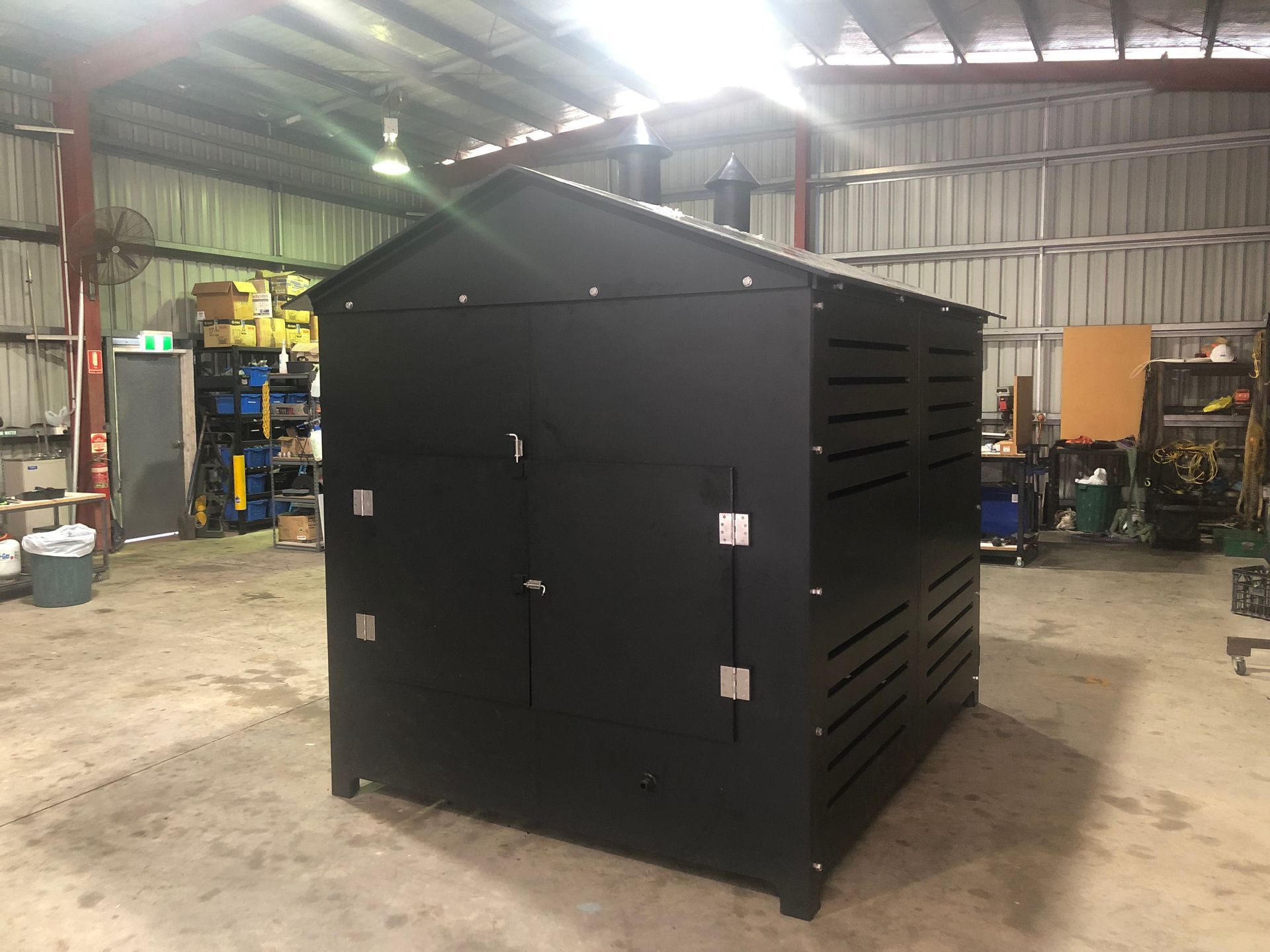 Large black metal equipment enclosure in a warehouse workshop, with slatted side panels and front doors. — Advanced Poly in Darwin, NT