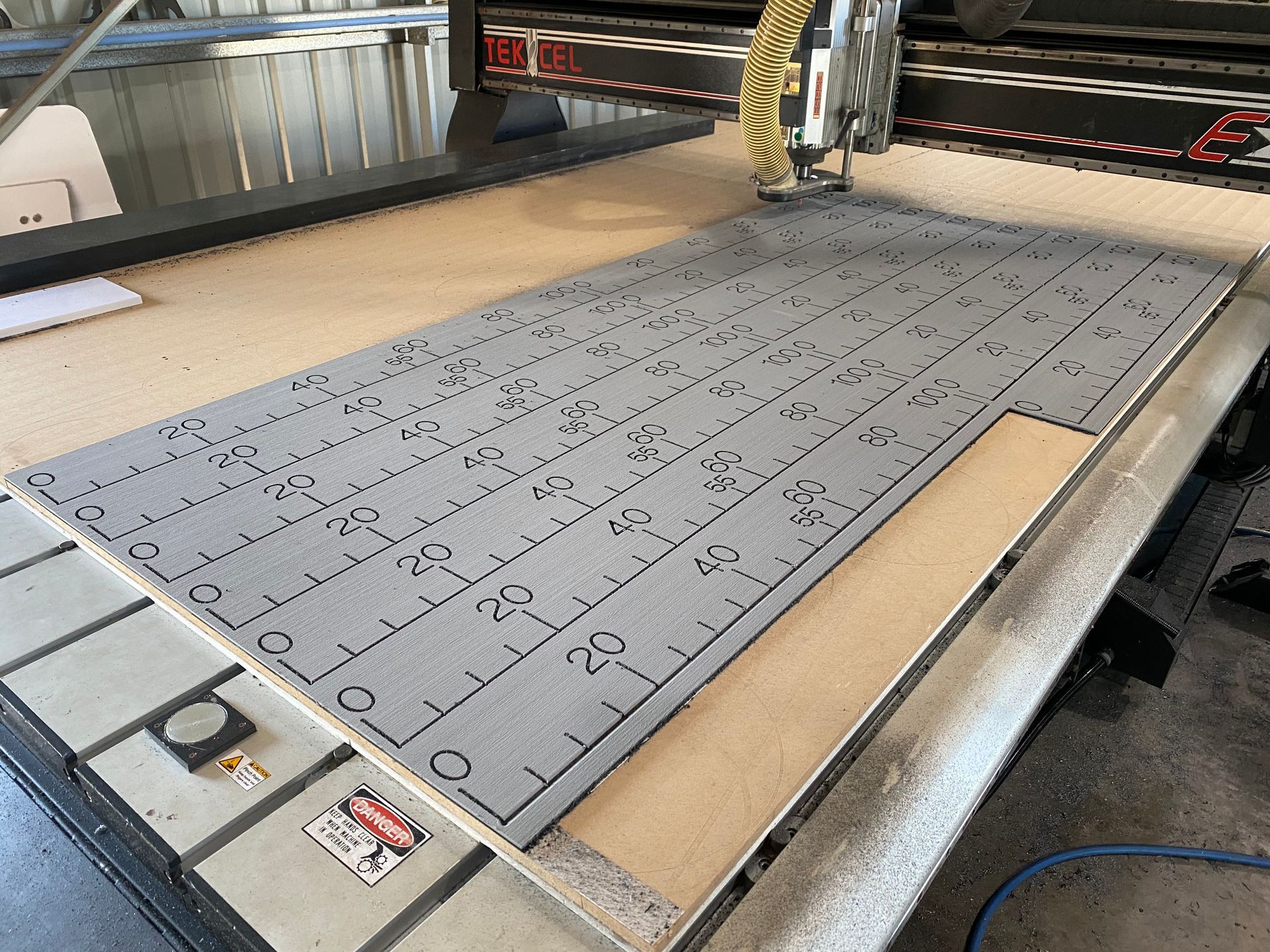 CNC router cutting a gray foam sheet on a workshop table, with a grid of parts marked on it. — Advanced Poly in Darwin, NT — Advanced Poly in Darwin, NT