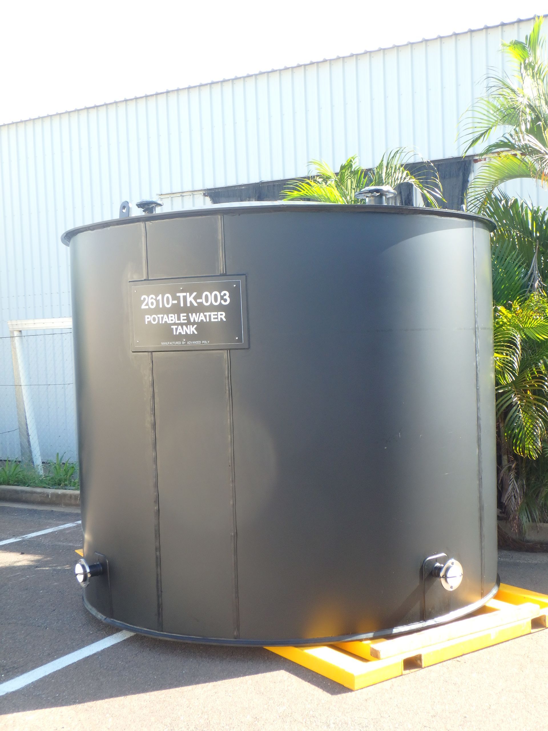 Large black cylindrical tank outdoors beside a corrugated metal building, with white markings and yellow chocks. — Advanced Poly in Darwin, NT