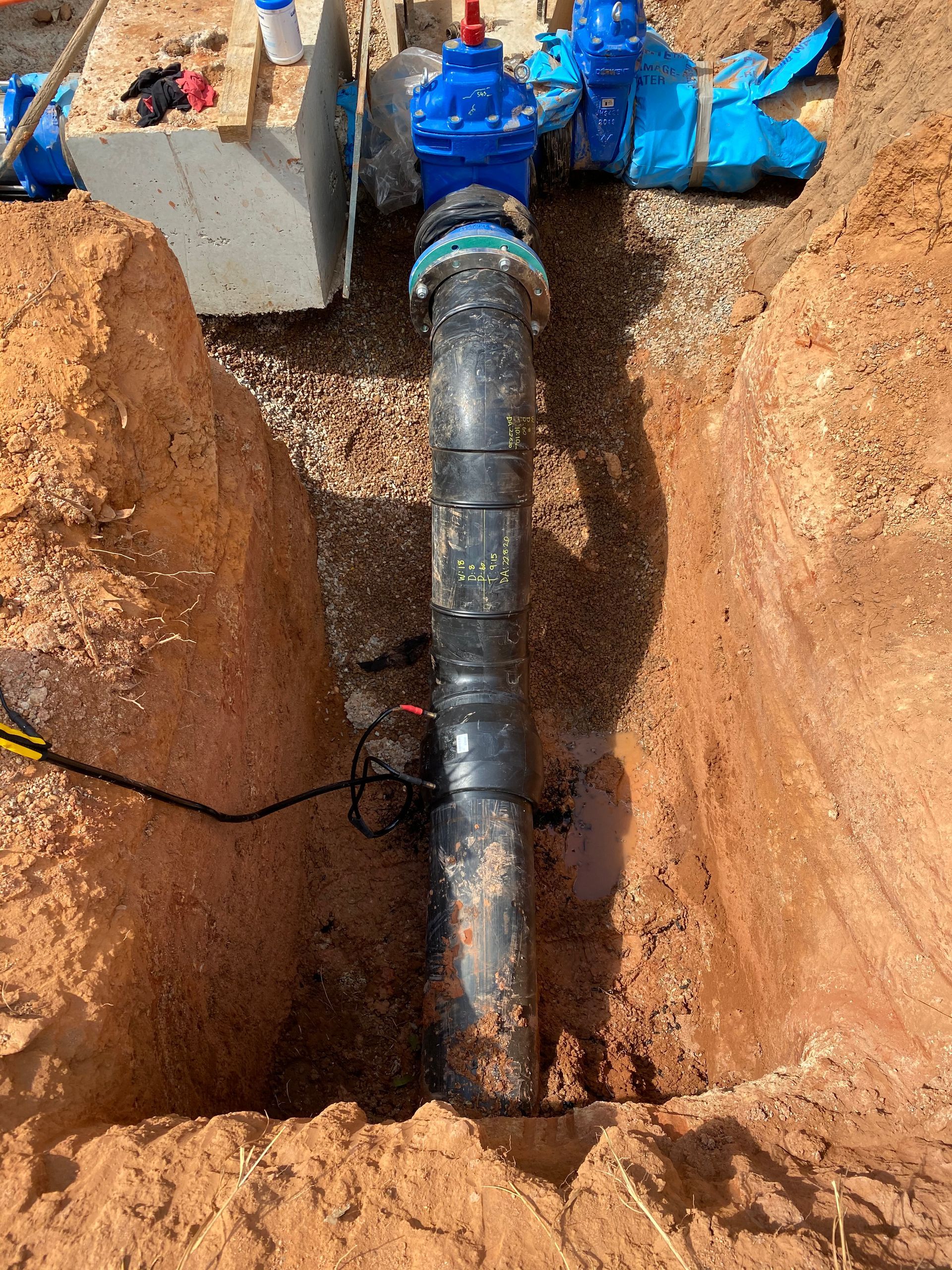 A trench with a black pipe repaired by blue couplings between dirt walls — Advanced Poly in Darwin, NT
