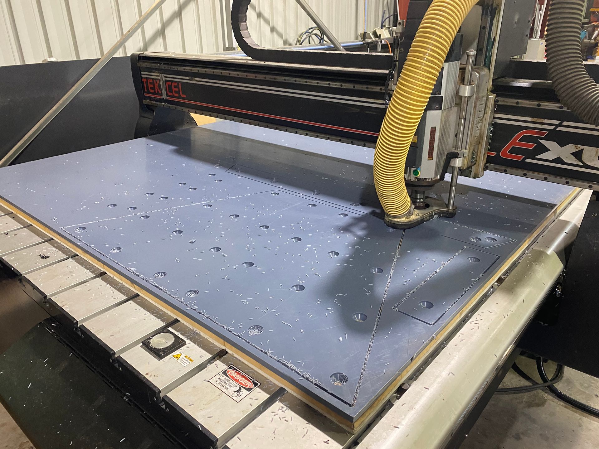 CNC router cutting a large blue sheet in a workshop, with yellow dust hose attached — Advanced Poly in Darwin, NT