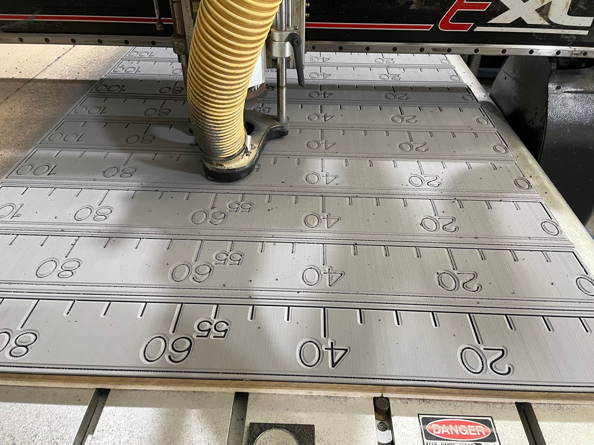 Close-up of a CNC machine cutting a silver metal sheet marked with measurements. — Advanced Poly in Darwin, NT