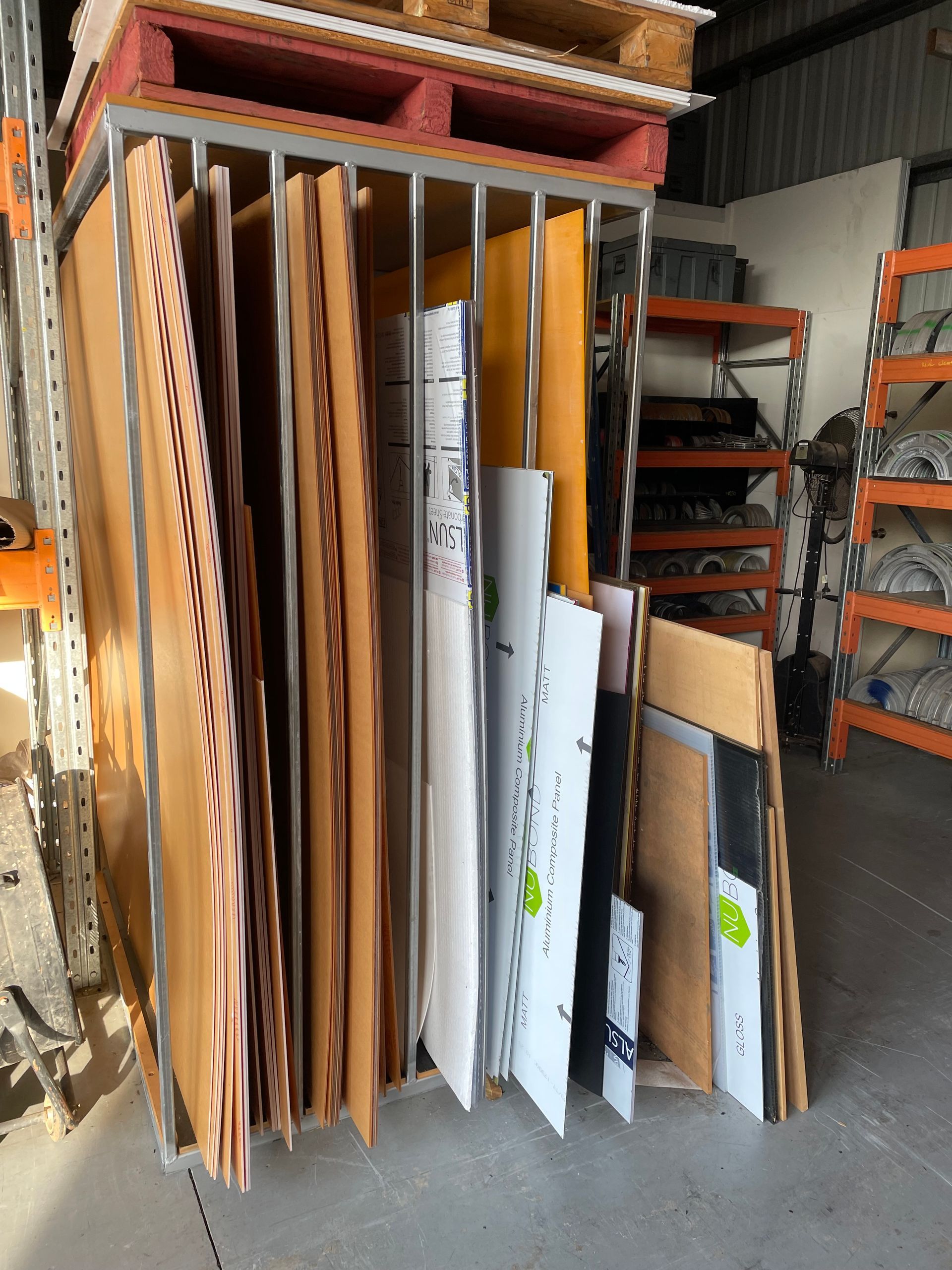 Stacked wooden boards and panels stored upright in an industrial warehouse aisle. — Advanced Poly in Darwin, NT