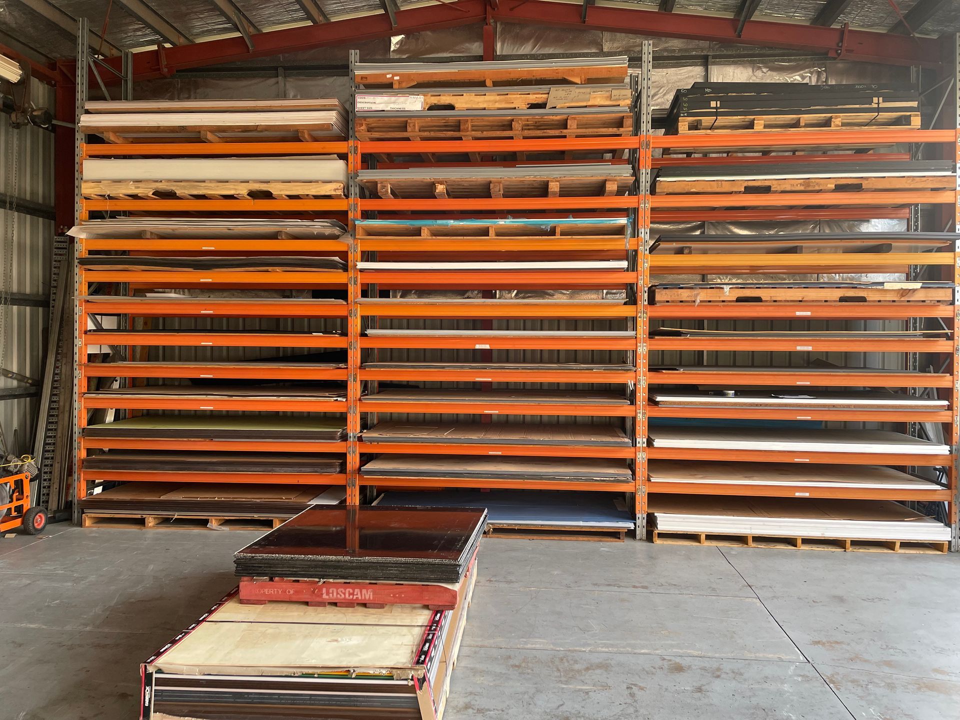 Warehouse with tall orange storage racks holding long metal sheets and panels — Advanced Poly in Darwin, NT