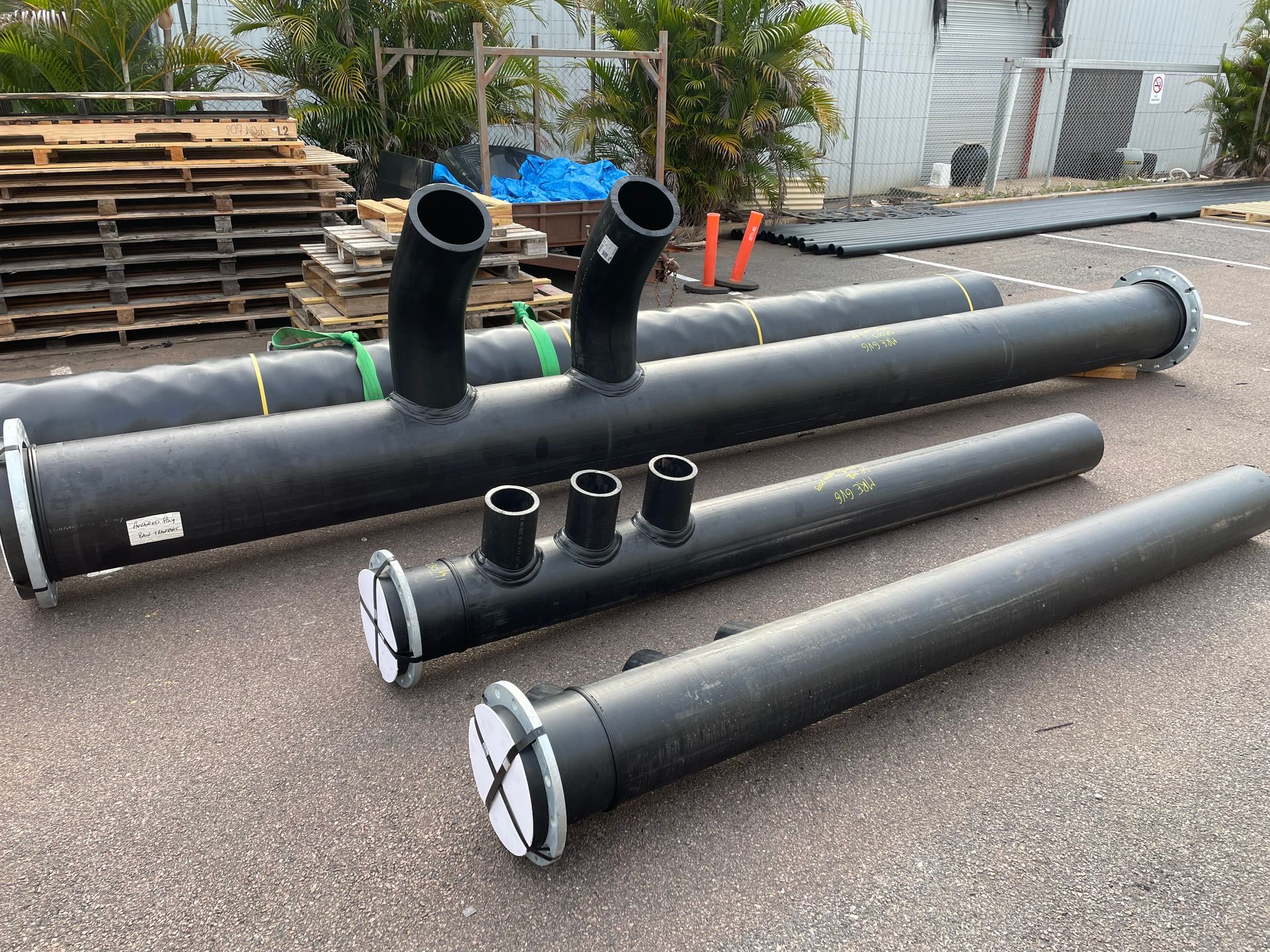 Black industrial pipes and fittings stacked outdoors on a pallet in a yard — Advanced Poly in Darwin, NT
